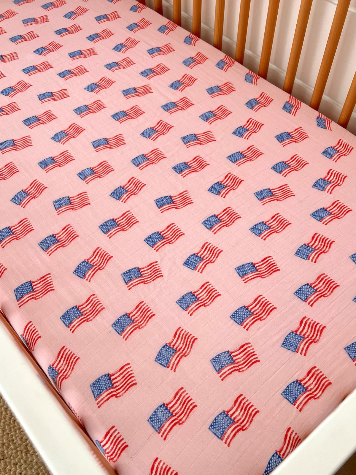 Baby crib mattress covered with a pink fabric featuring a pattern of American flags.