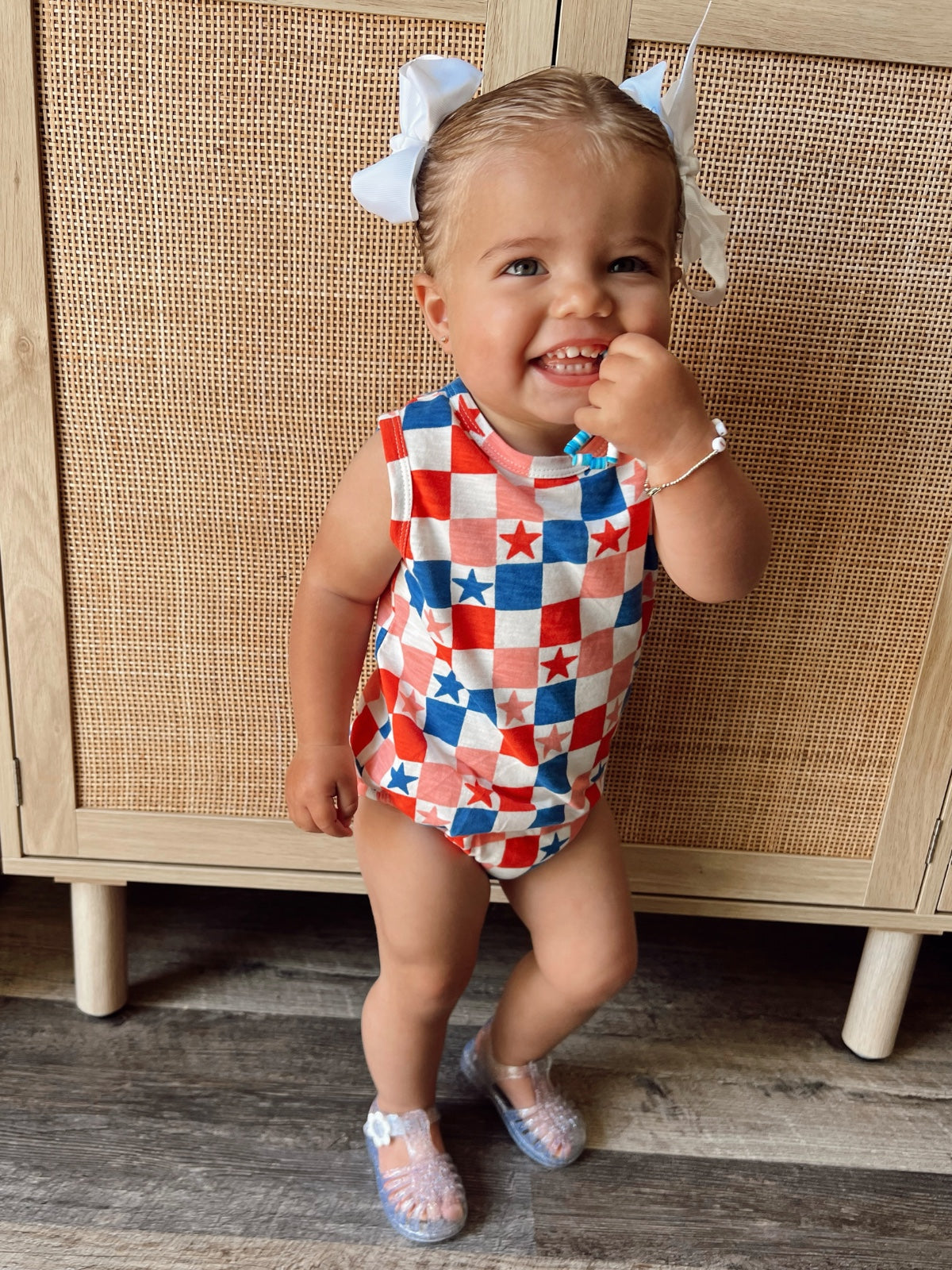 Smiling toddler in a colorful star-patterned outfit, standing next to a wooden cabinet.