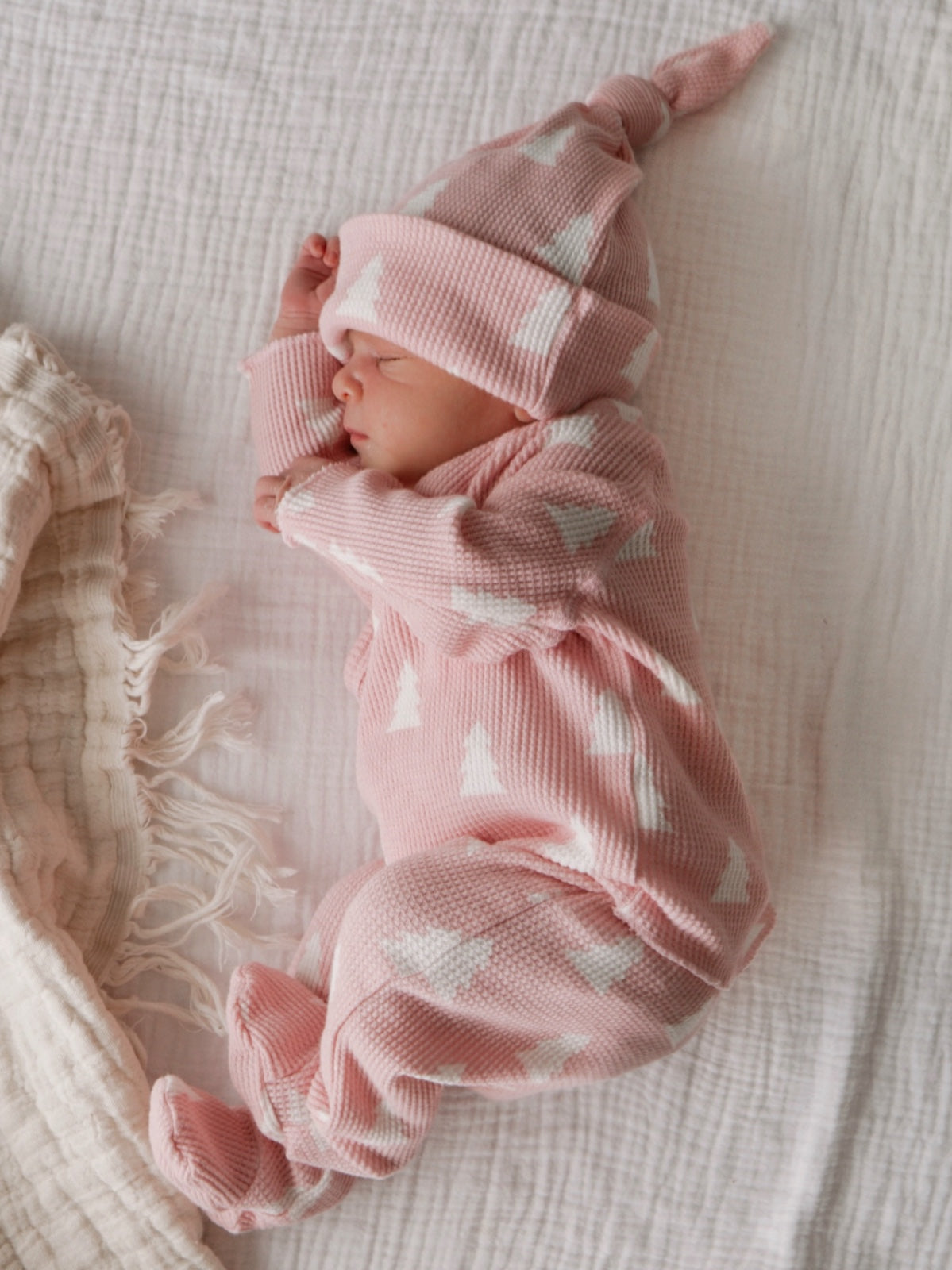 Newborn baby dressed in a pink outfit with white patterns, peacefully sleeping on a textured blanket.