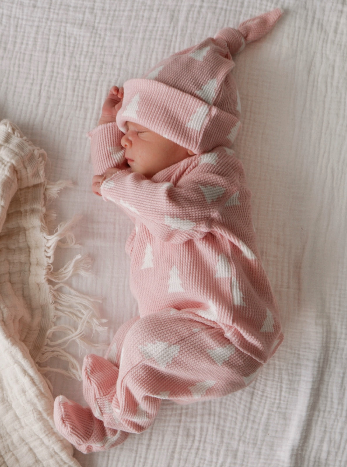 Newborn baby dressed in a pink outfit with white patterns, peacefully sleeping on a textured blanket.