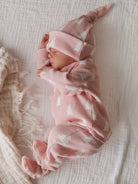 Newborn baby dressed in a pink outfit with white patterns, peacefully sleeping on a textured blanket.