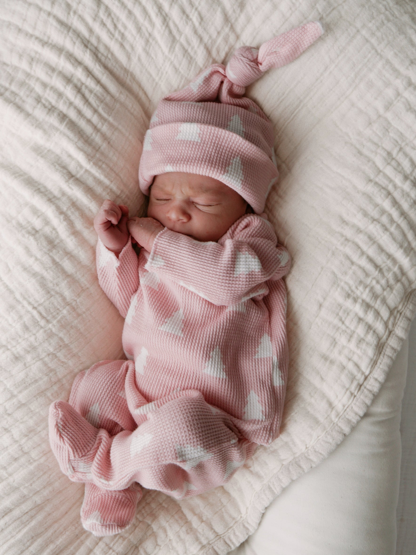 Newborn baby girl in a pink outfit with white patterns, sleeping on a soft blanket.