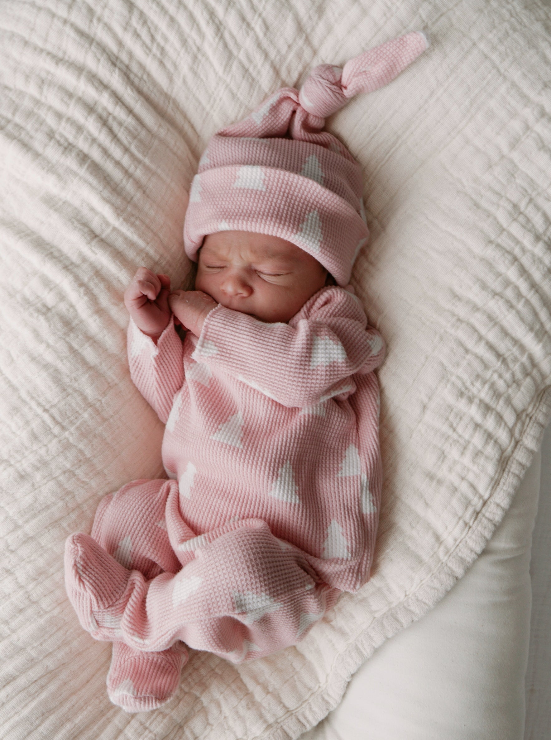 Newborn baby girl in a pink outfit with white patterns, sleeping on a soft blanket.