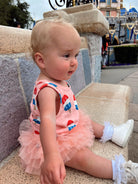 Toddler sitting on a stone bench, wearing a colorful outfit with a tulle skirt, at a theme park.
