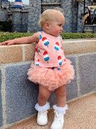 Toddler in playful outfit with popsicle prints, posing near a castle backdrop.