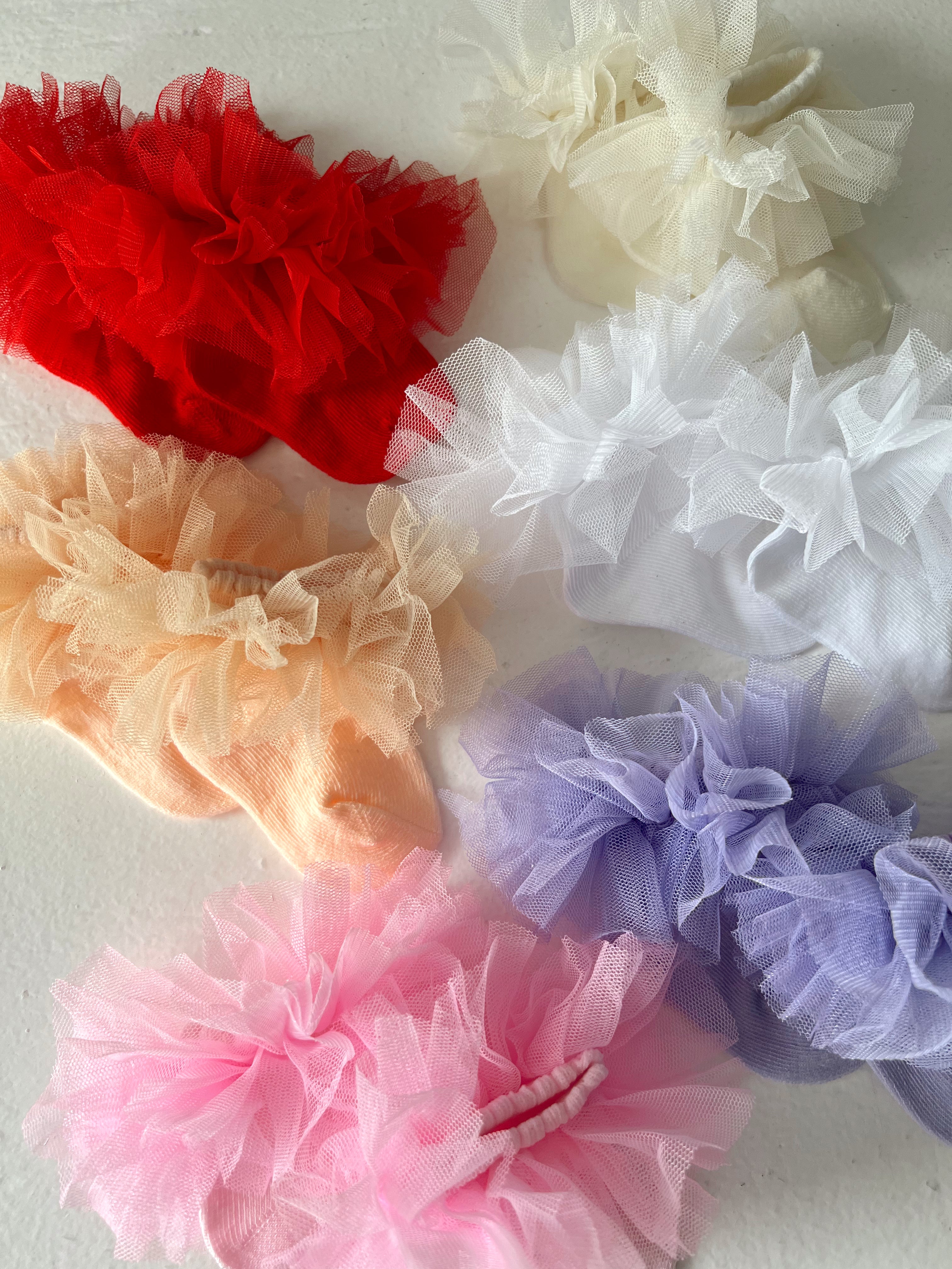 Colorful tulle hair accessories in red, peach, pink, purple, white, and cream arranged on a light background.