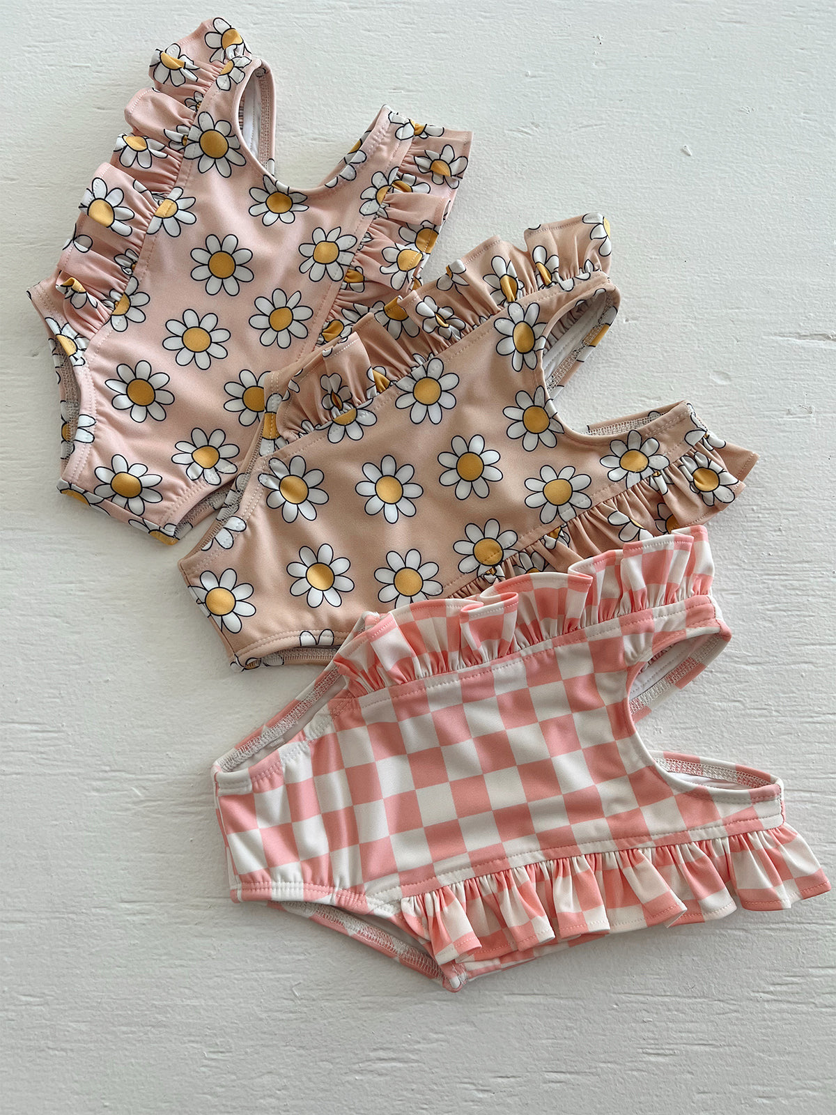 Three baby swimsuits featuring floral and checkered patterns on a light background.