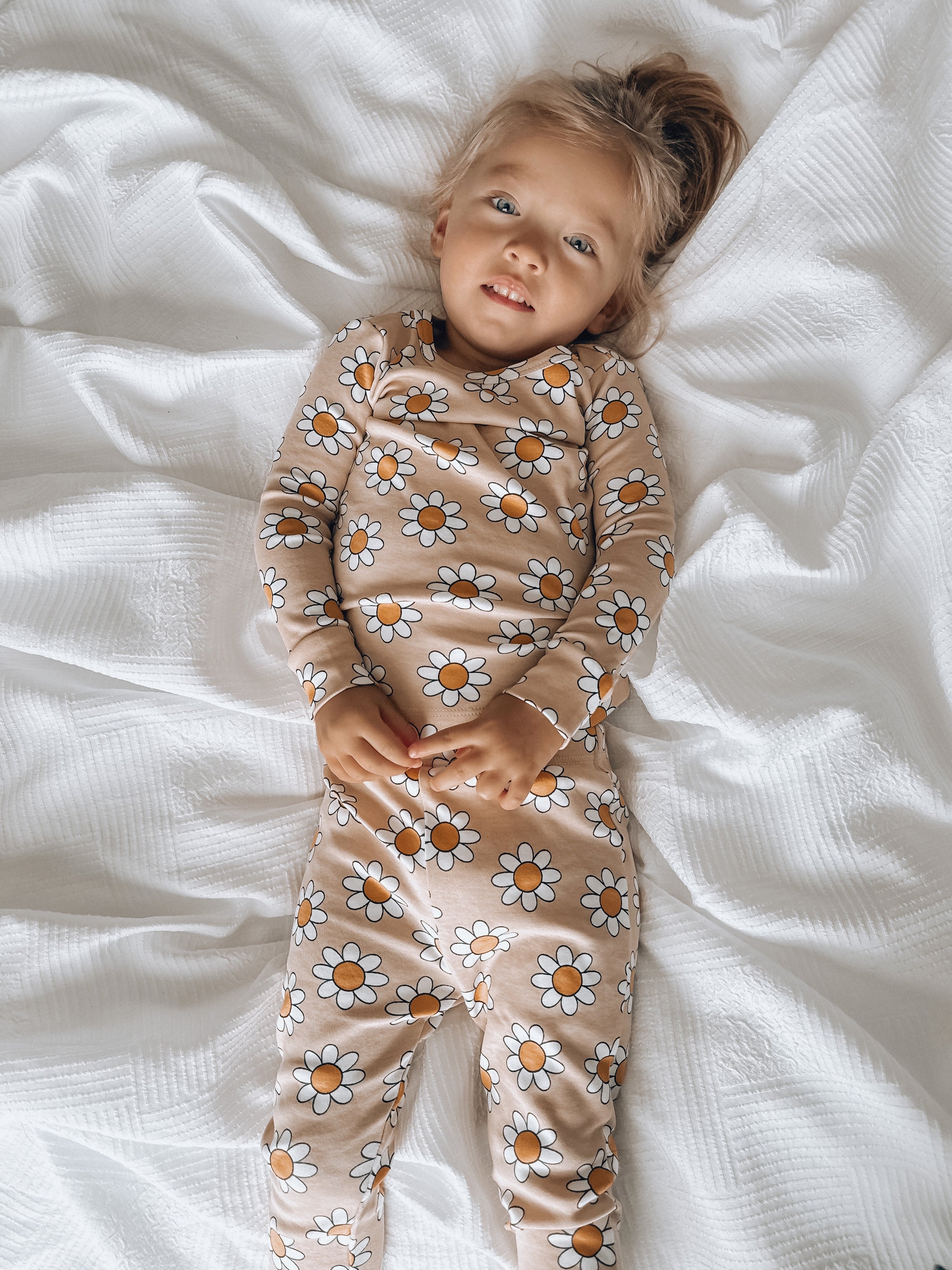 Young child in floral pajamas lying on a white blanket, smiling at the camera.