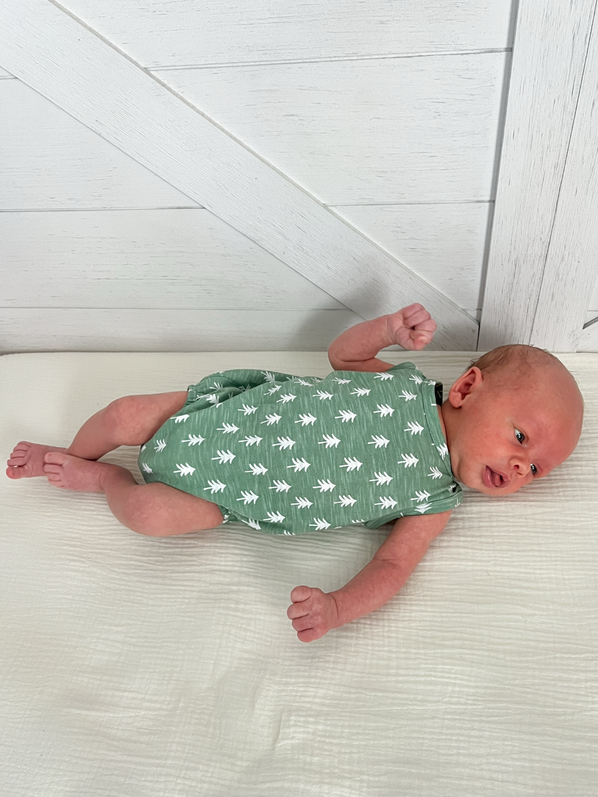 Newborn wearing a green onesie with white leaf patterns, lying on a light background.