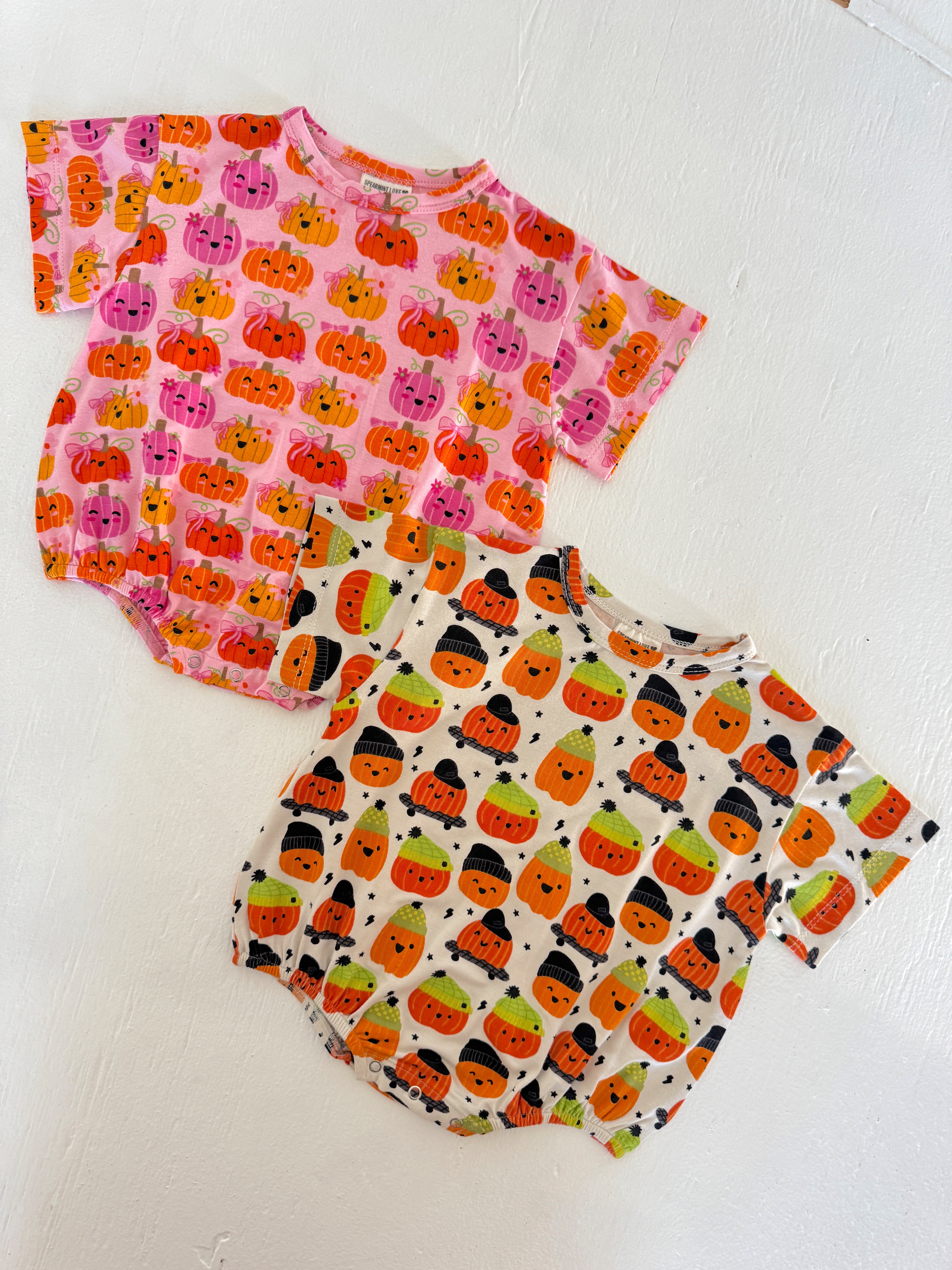 Two cute baby bodysuits with colorful pumpkin prints, one pink and one cream, displayed on a white surface.