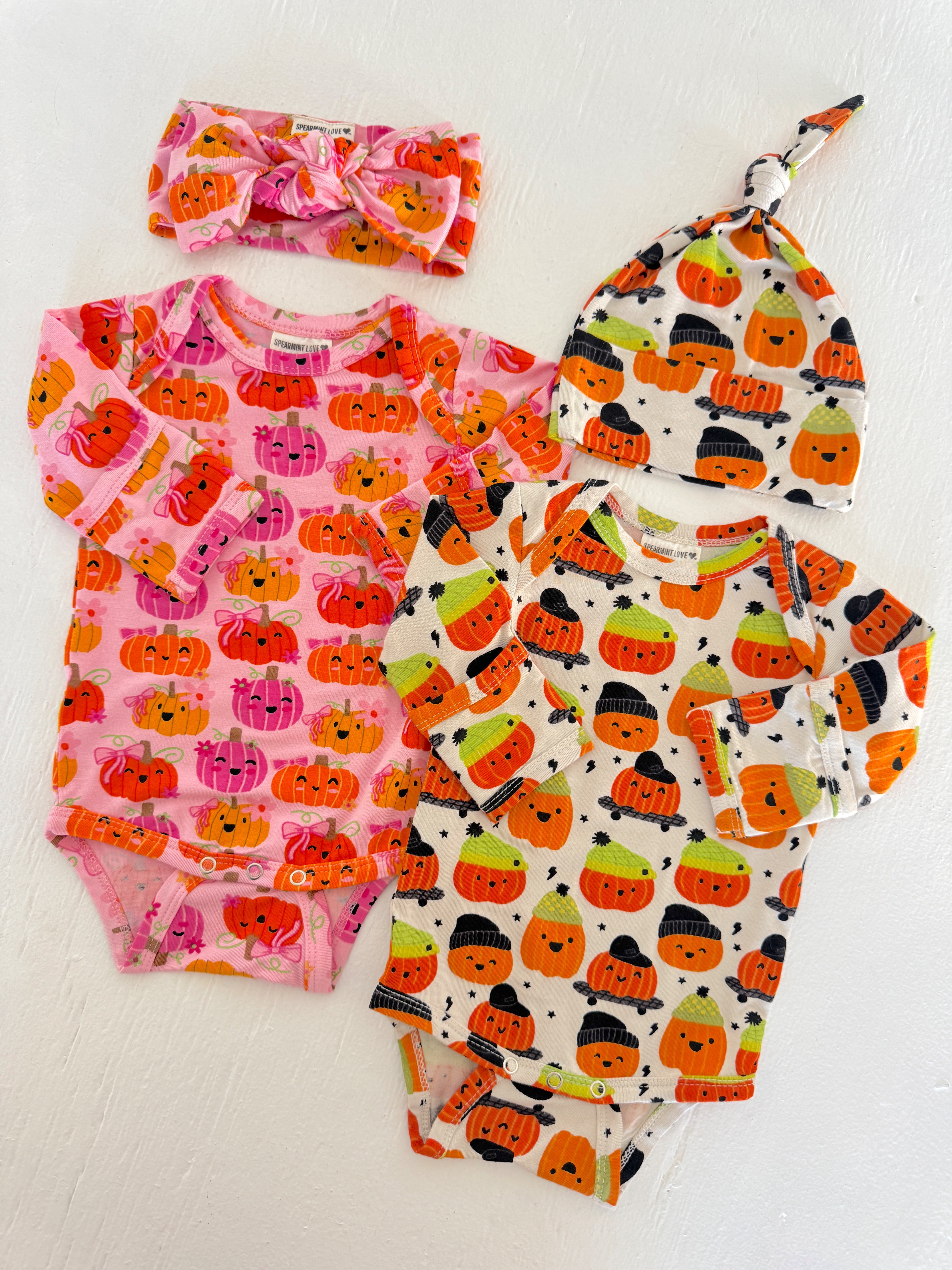 Colorful baby outfits featuring pumpkin patterns, including a headband and hat, on a light background.