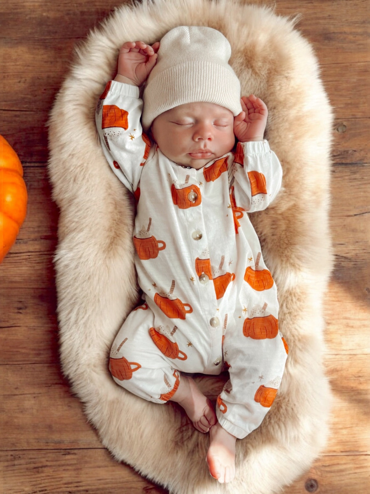 Sleeping baby in cozy pumpkin-themed outfit on a fluffy blanket, surrounded by autumn decor.
