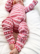 Baby in a pink striped onesie with red hearts, lying on a white blanket, raising arms playfully.