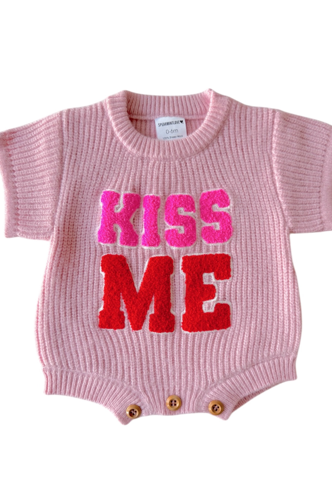 Pink baby romper with "KISS ME" in bold, colorful letters at the front. Short sleeves and button closure at the bottom.