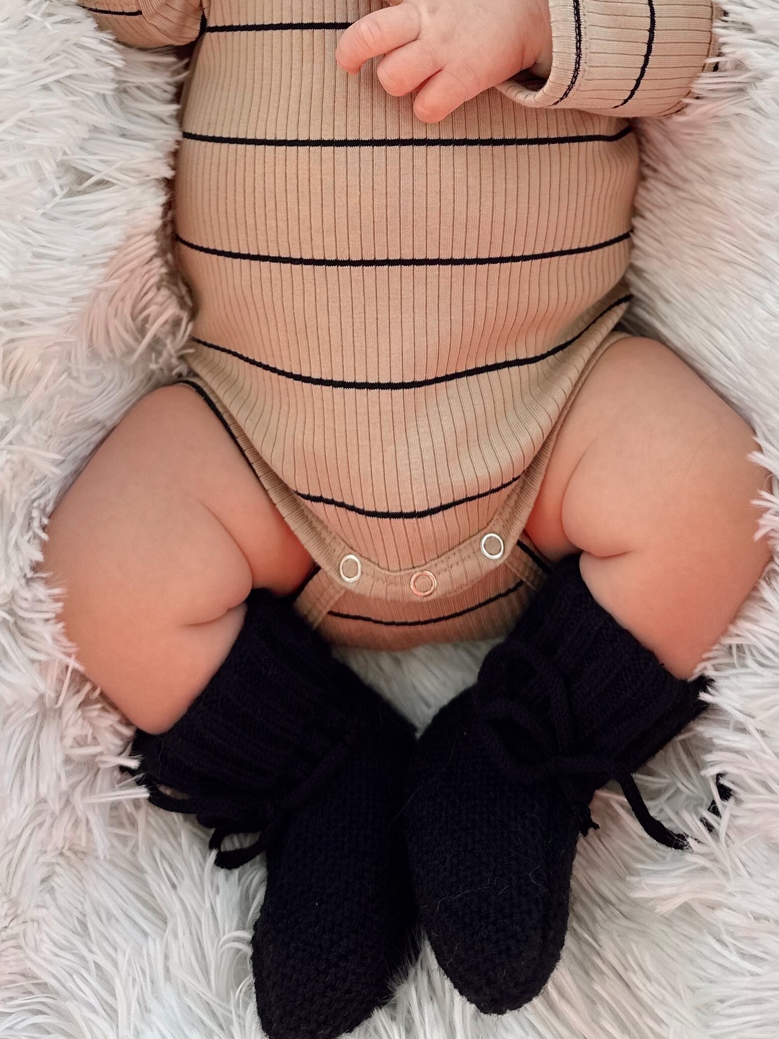 Close-up of a baby in a striped bodysuit and black knitted booties, resting on a fluffy blanket.