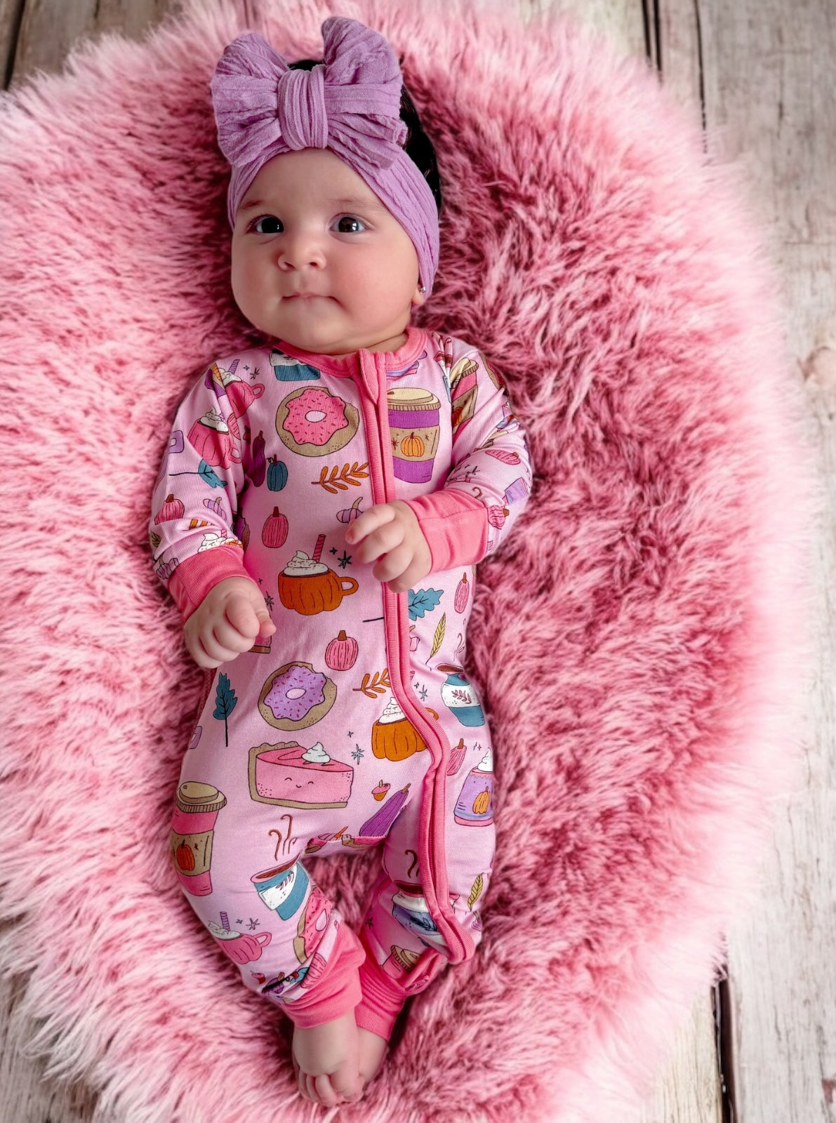 Baby wearing a vibrant pink onesie with dessert patterns, resting on a fluffy pink blanket.