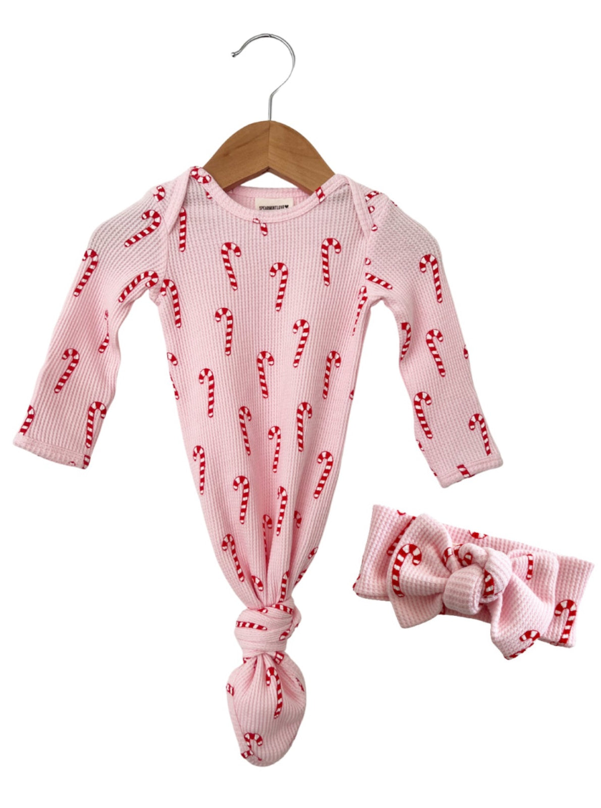 Pink onesie with candy cane print and matching headband, both displayed on a wooden hanger.