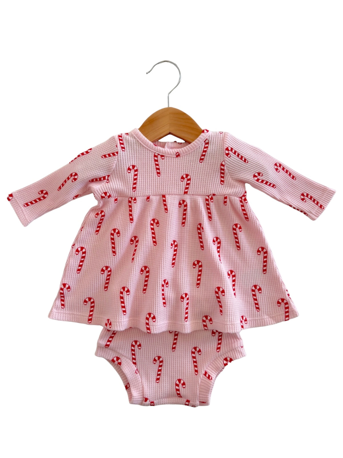 Pink dress with candy cane pattern, featuring long sleeves and attached diaper cover, displayed on a wooden hanger.