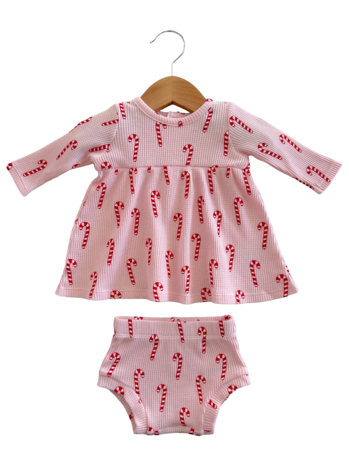 Candy cane patterned pink dress and matching shorts, hanging on a wooden hanger. Perfect for festive occasions.