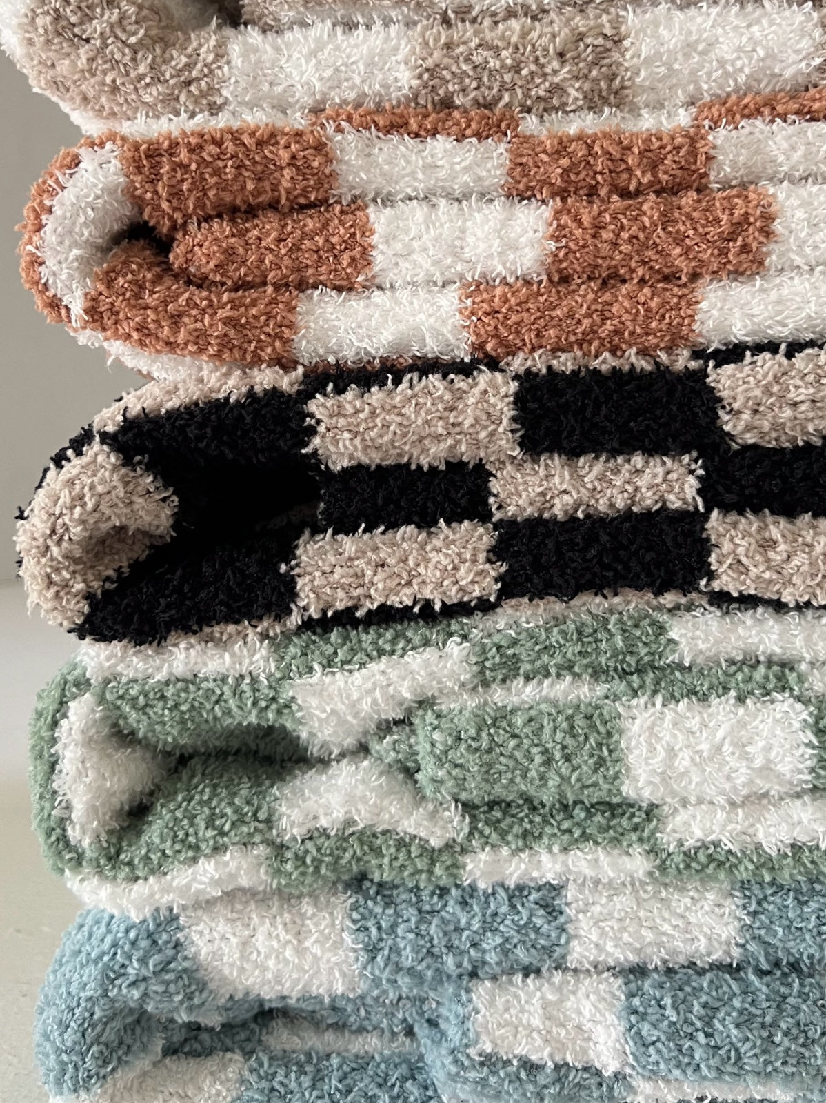 Stacked plush towels in various colors and patterns, featuring soft textures and a cozy aesthetic.