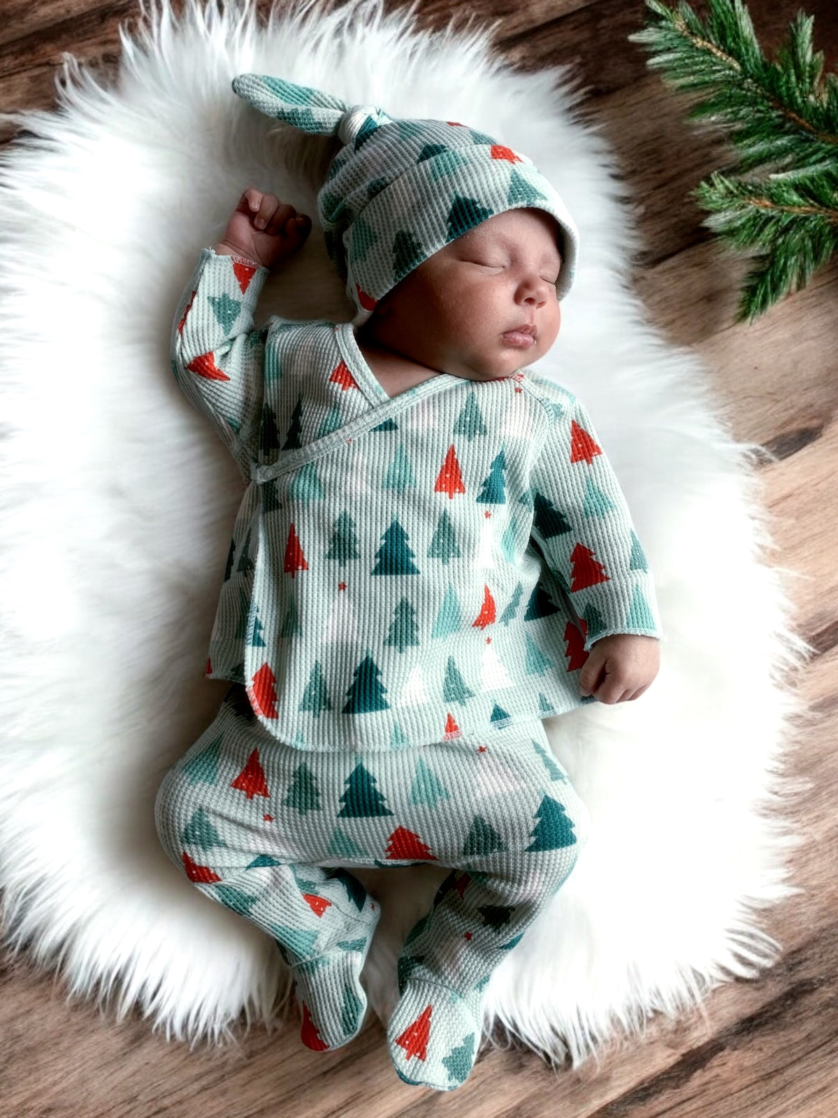 Baby peacefully sleeping on a soft rug, dressed in a festive, tree-patterned outfit and matching hat.