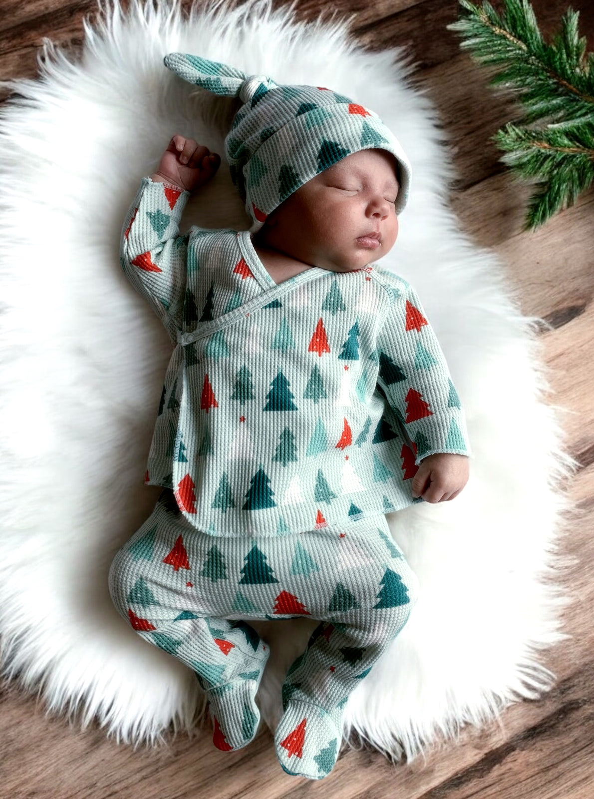 Baby peacefully sleeping on a soft rug, dressed in a festive, tree-patterned outfit and matching hat.