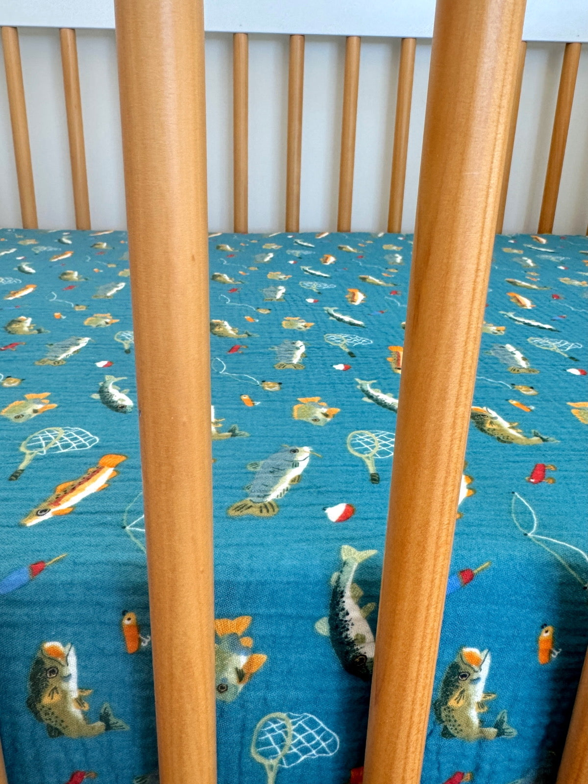 Wooden crib with a blue fabric sheet featuring colorful fish and fishing motifs.