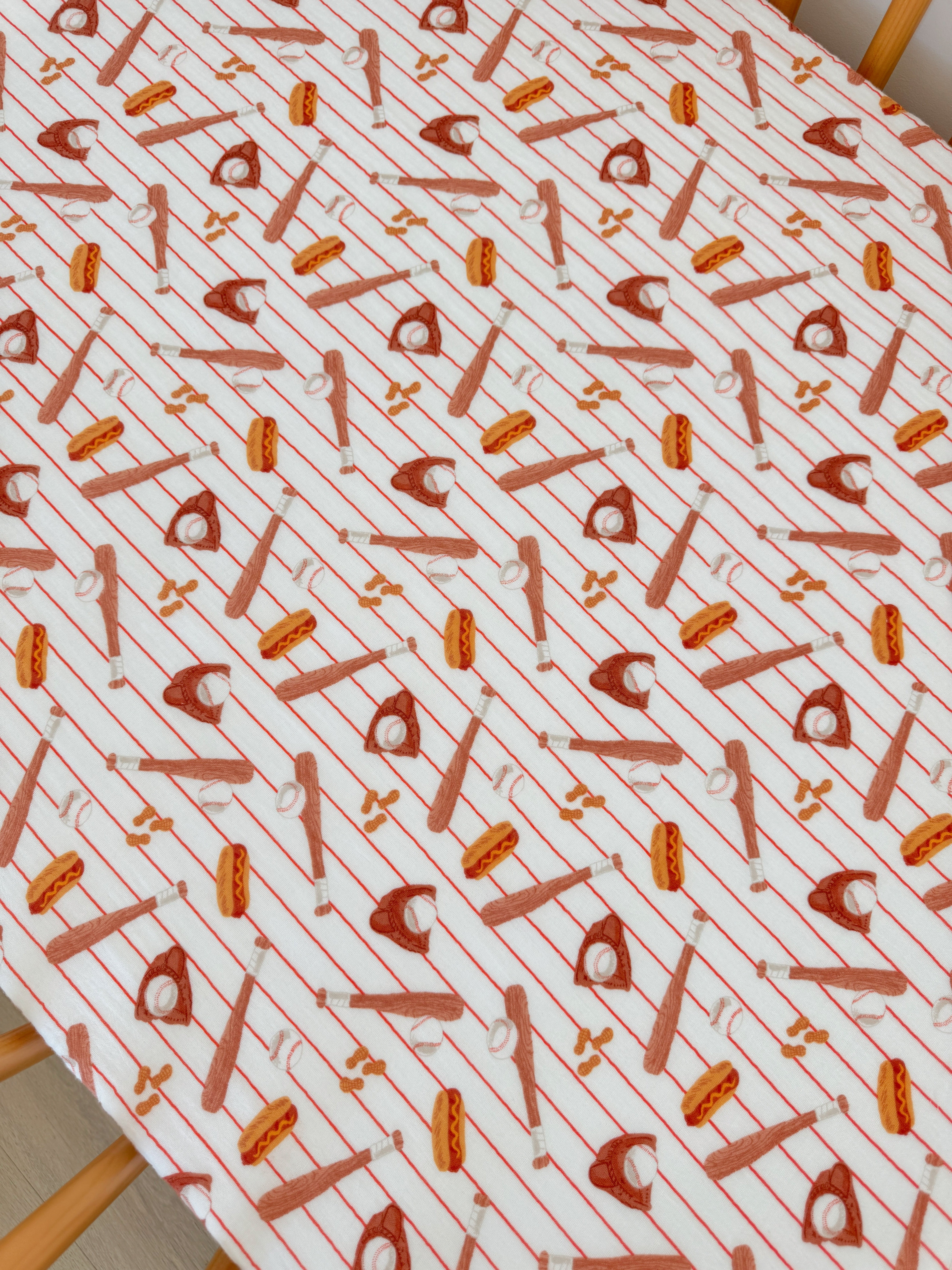 Patterned fabric featuring various baseball-related items like bats, balls, and hot dogs on a striped background.