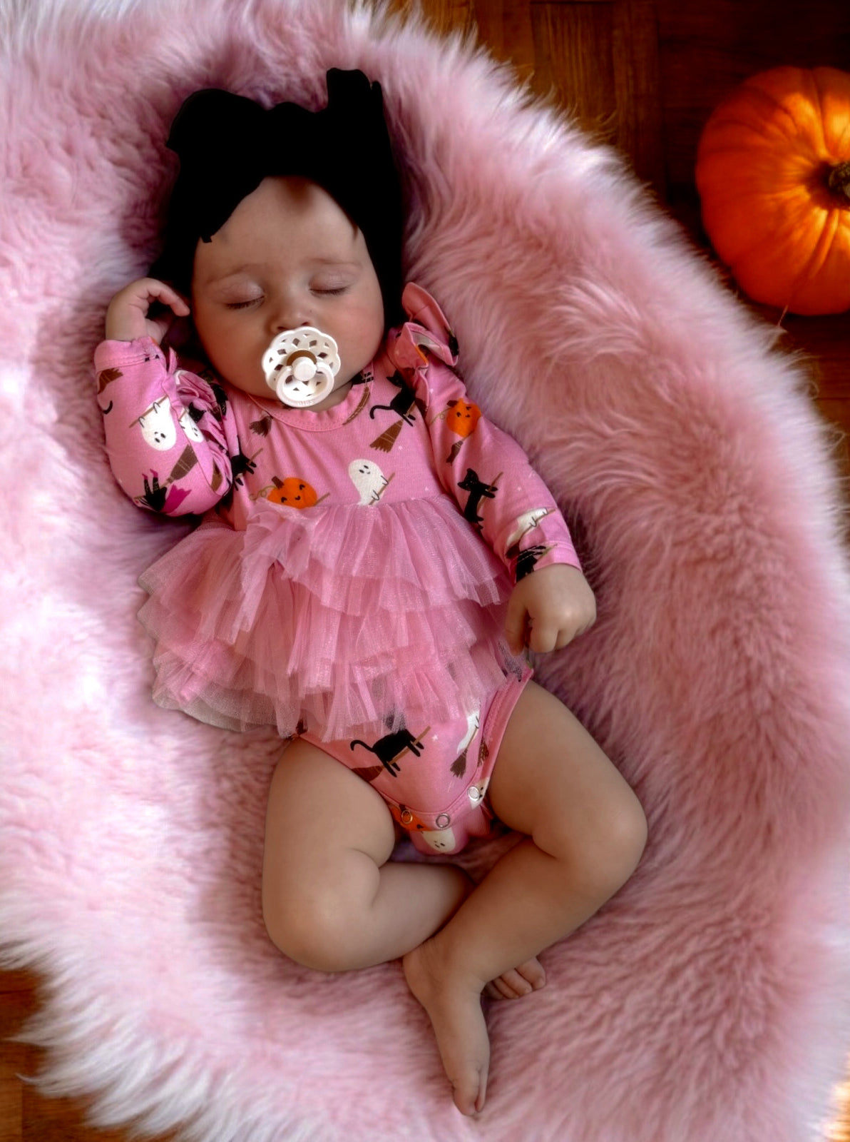 Baby girl in pink outfit with lace, sleeping on fluffy blanket, with a pumpkin in the background.