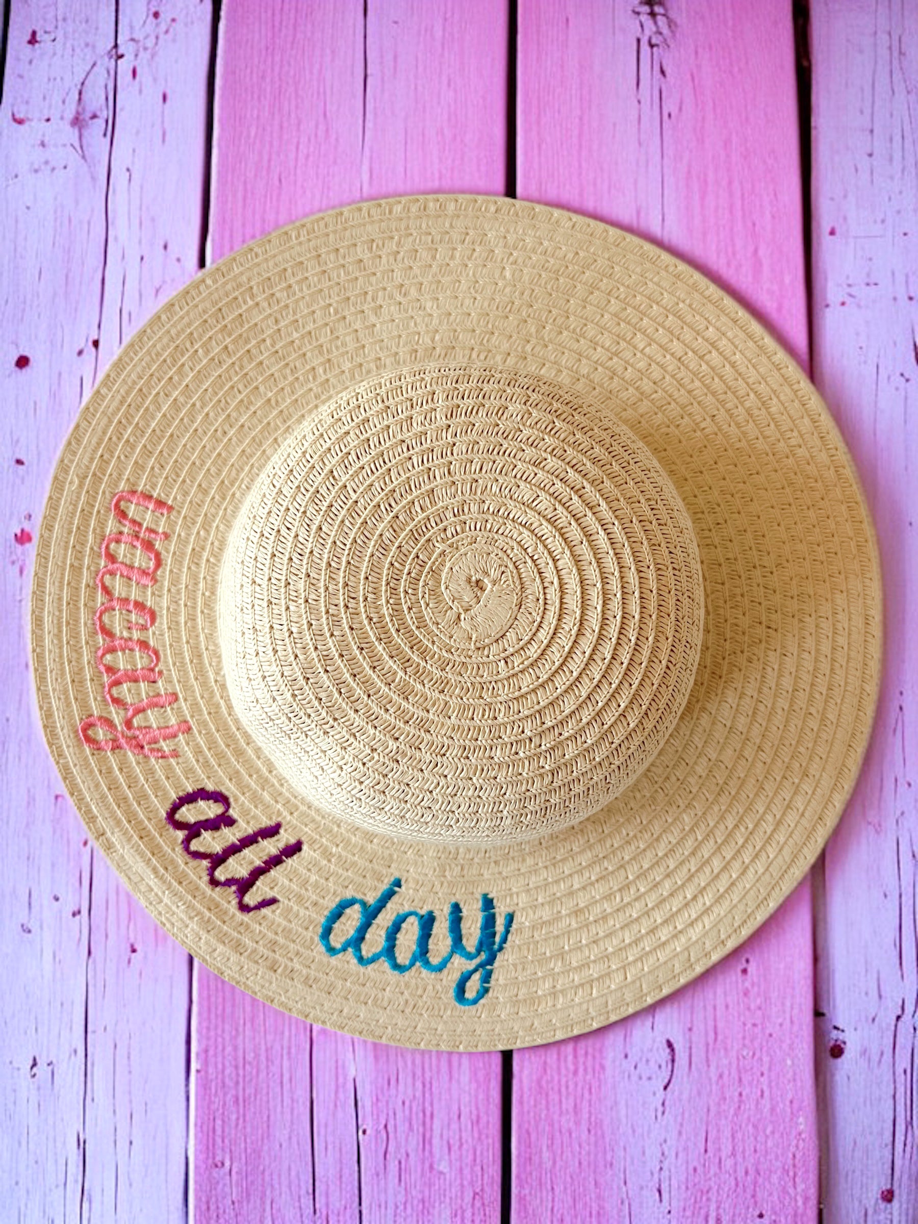 Wide-brim straw hat with "vacay all day" text, resting on a pink wooden background. Perfect for summer outings.