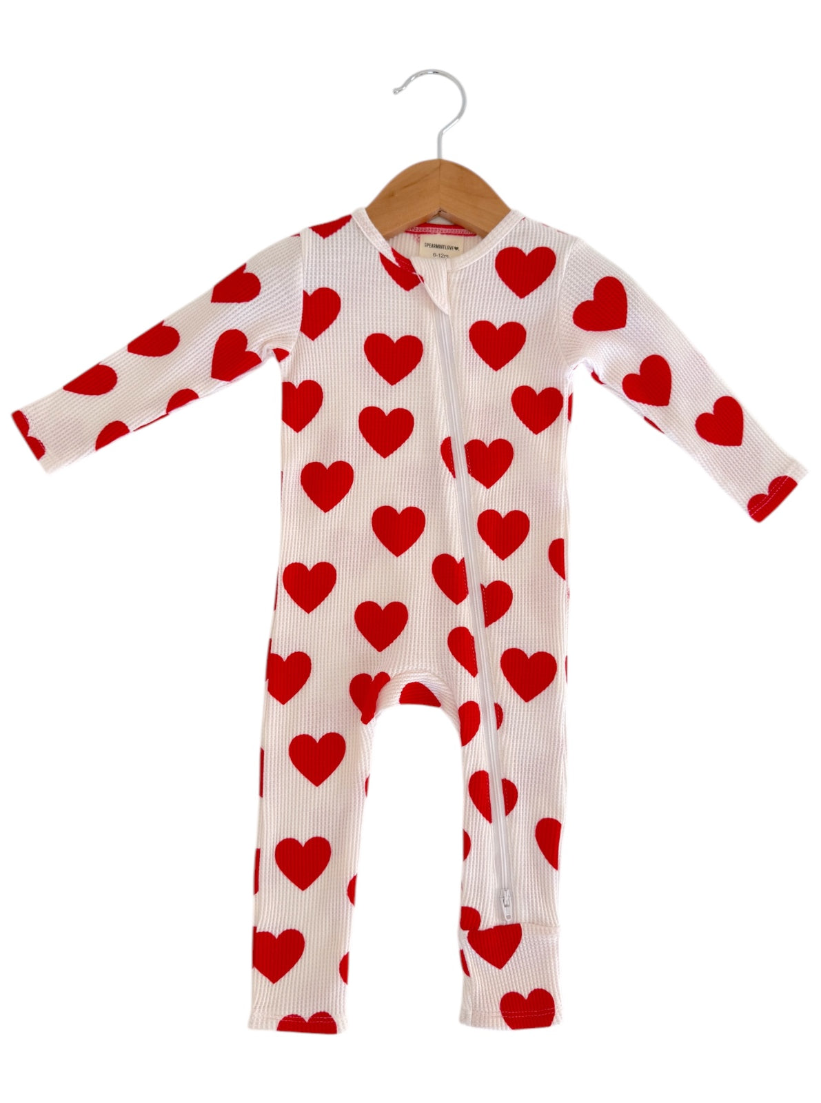 White onesie with red heart patterns, hanging on a wooden hanger against a plain background.