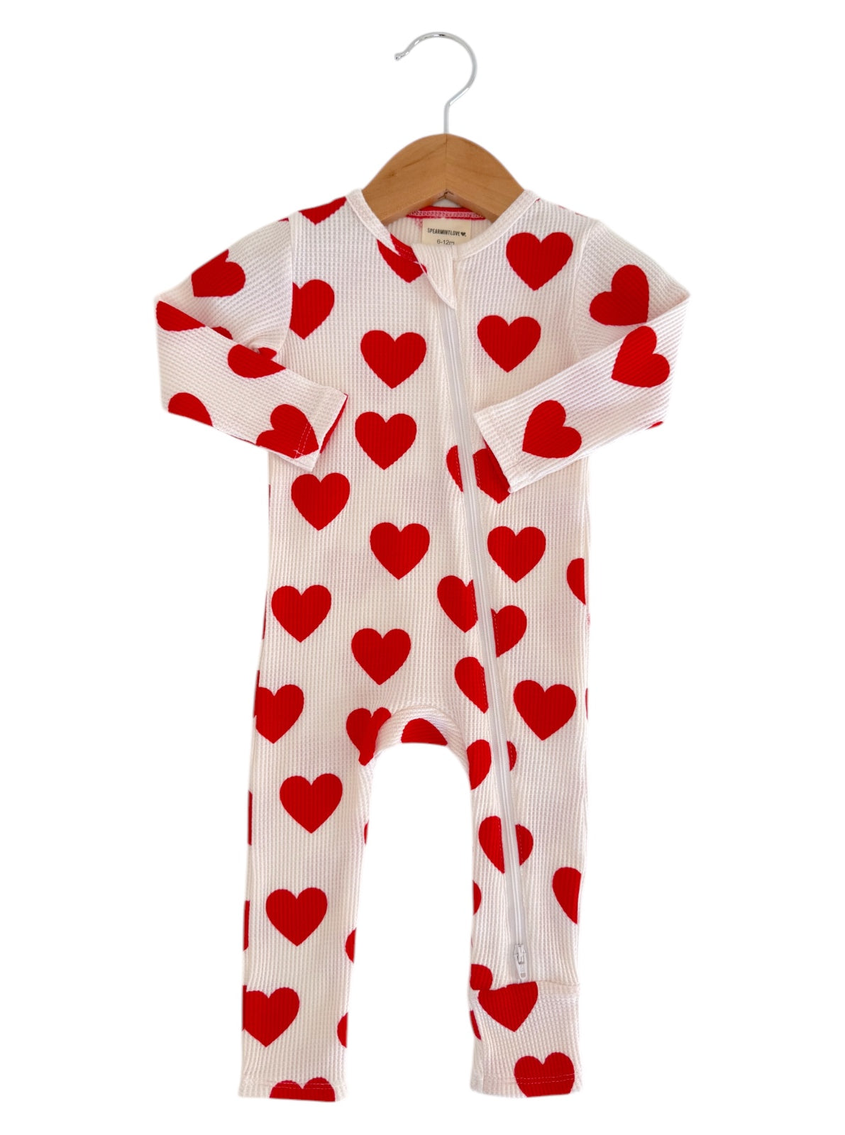 White onesie with red heart patterns, hanging on a wooden hanger.