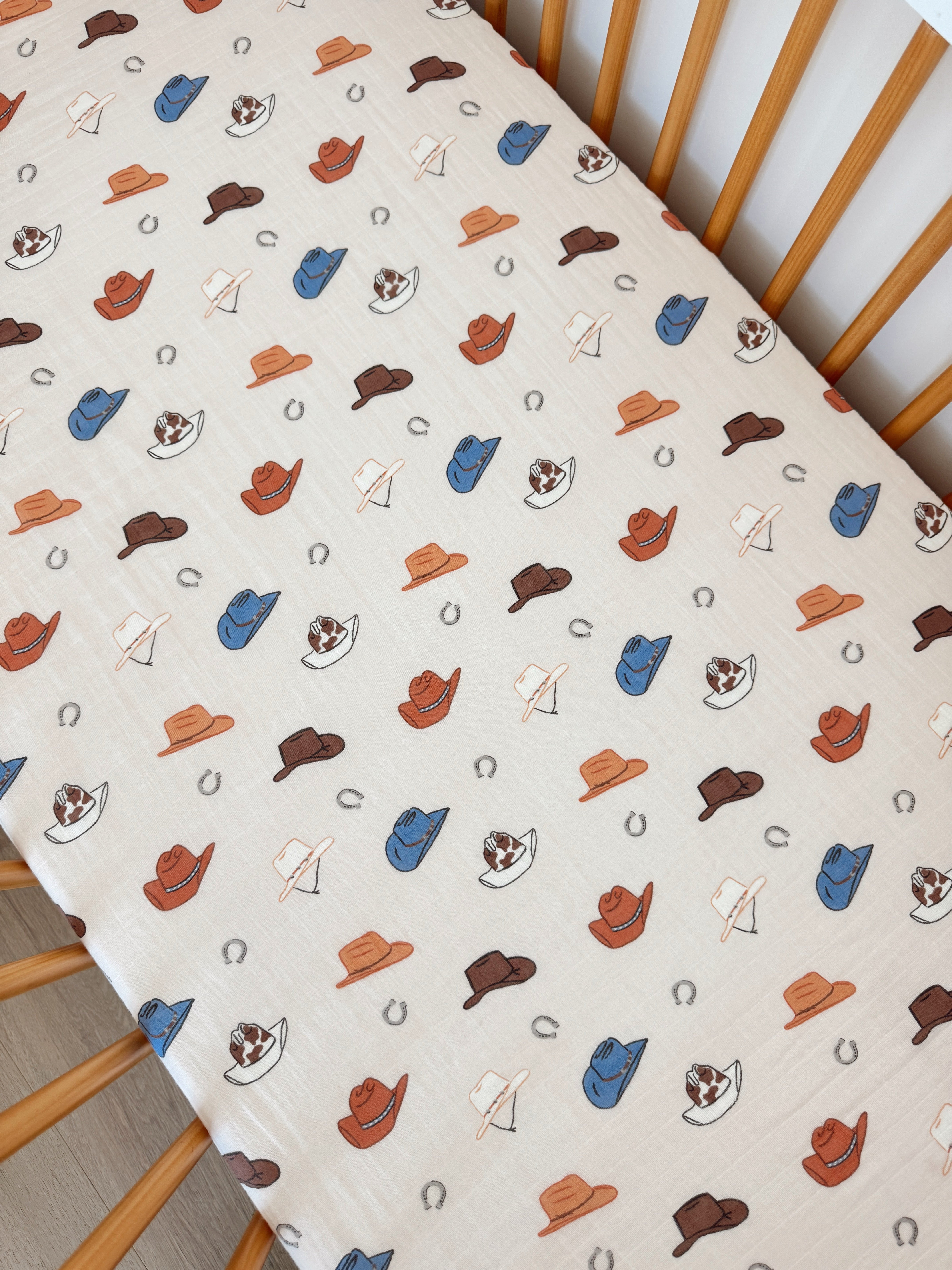 Colorful fabric featuring various hats and horseshoes on a light background, perfect for a playful nursery theme.