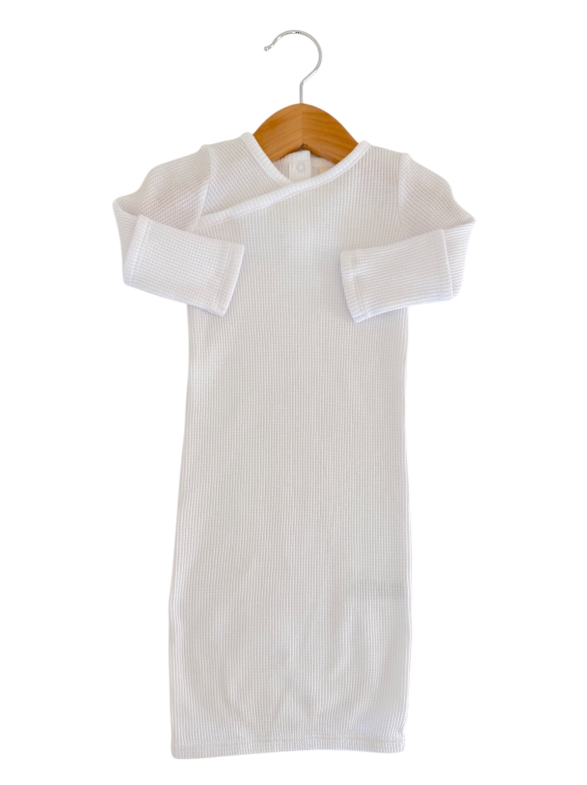 White ribbed baby dress hanging on a wooden hanger against a plain background.
