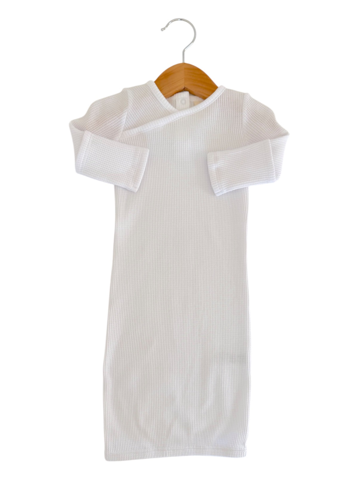 White ribbed baby dress hanging on a wooden hanger against a plain background.