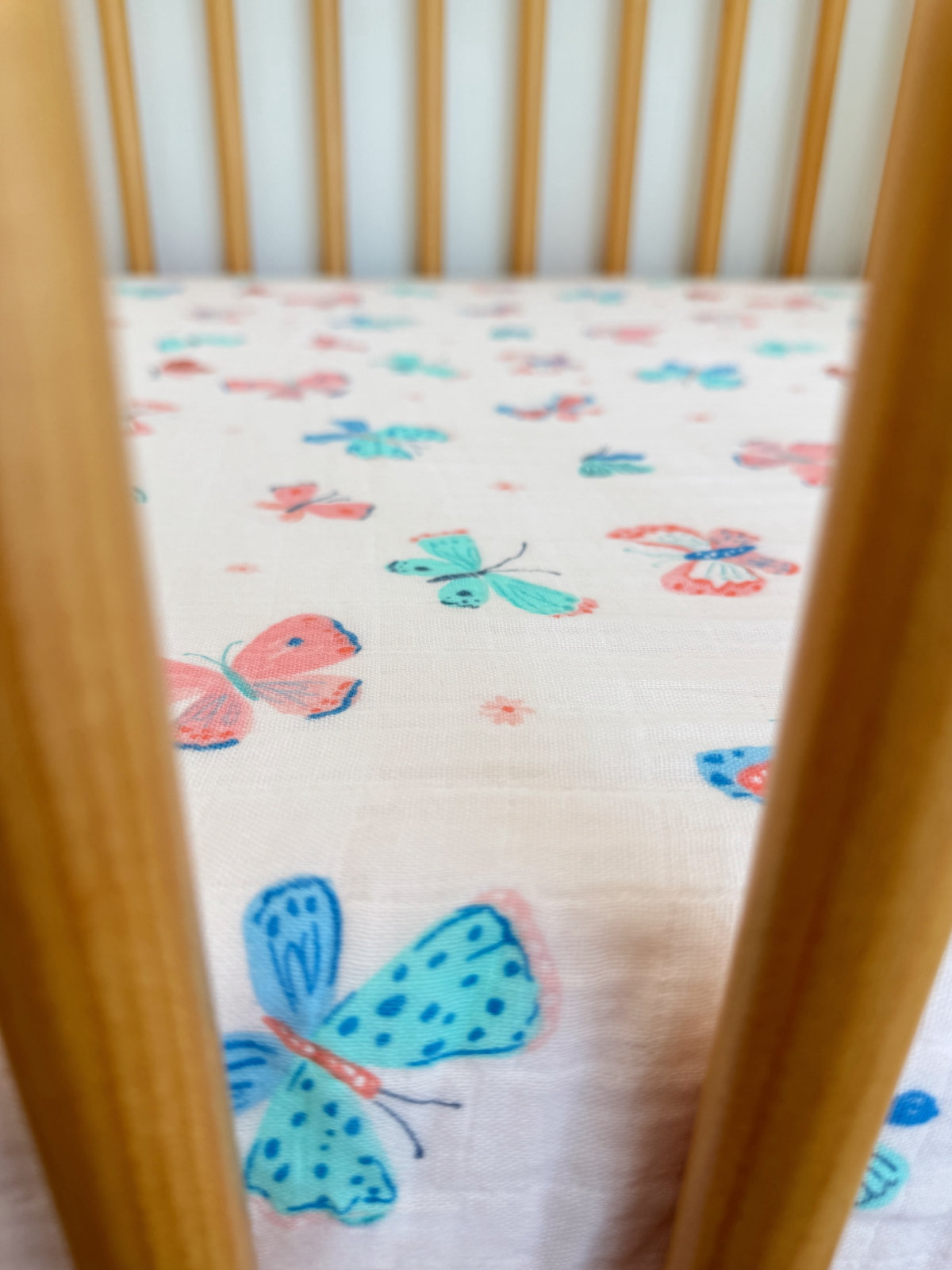 Colorful butterfly pattern on a crib sheet seen through wooden crib bars.