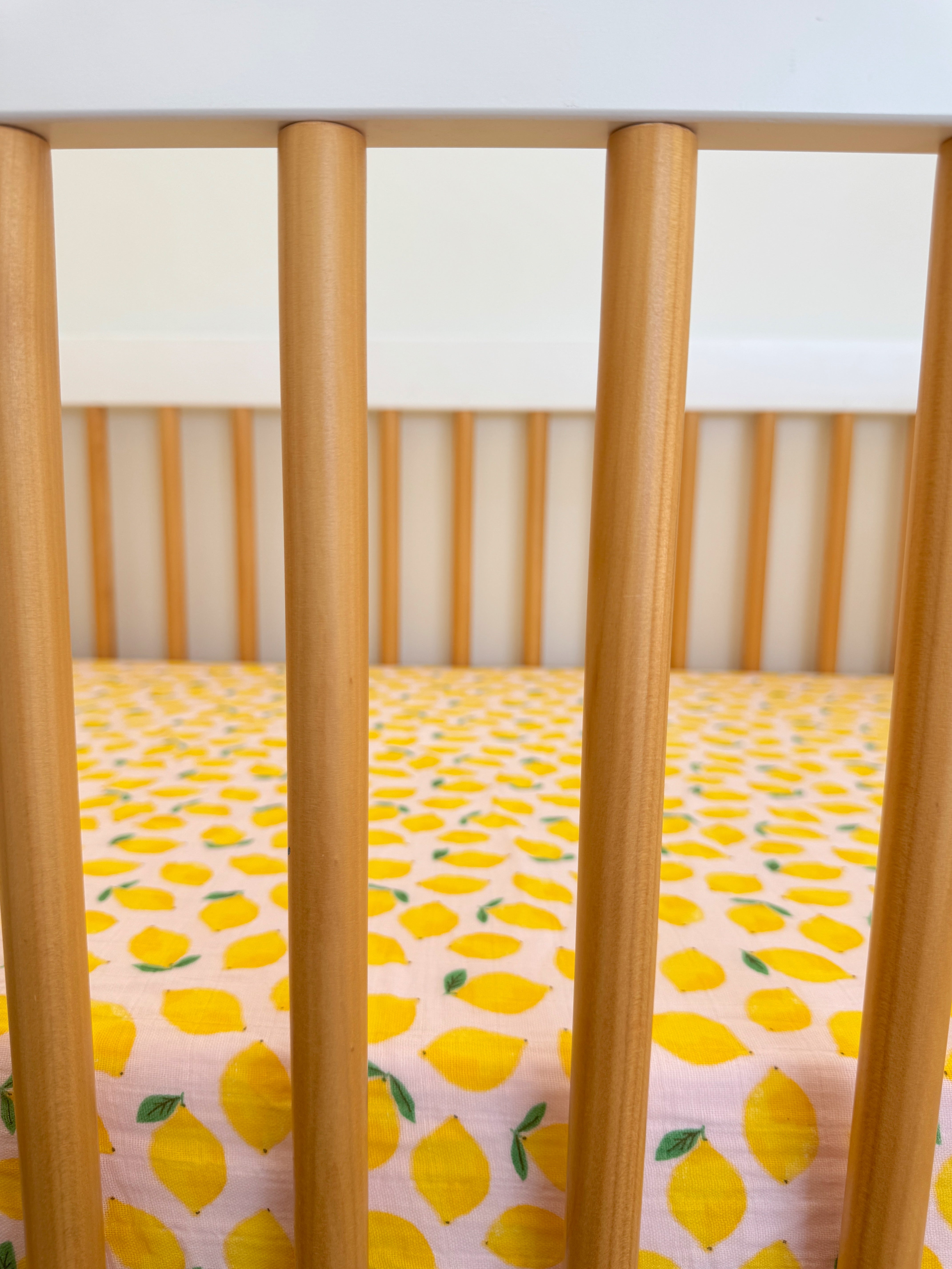 Crib with wooden bars and a pink sheet featuring a lemon pattern inside.