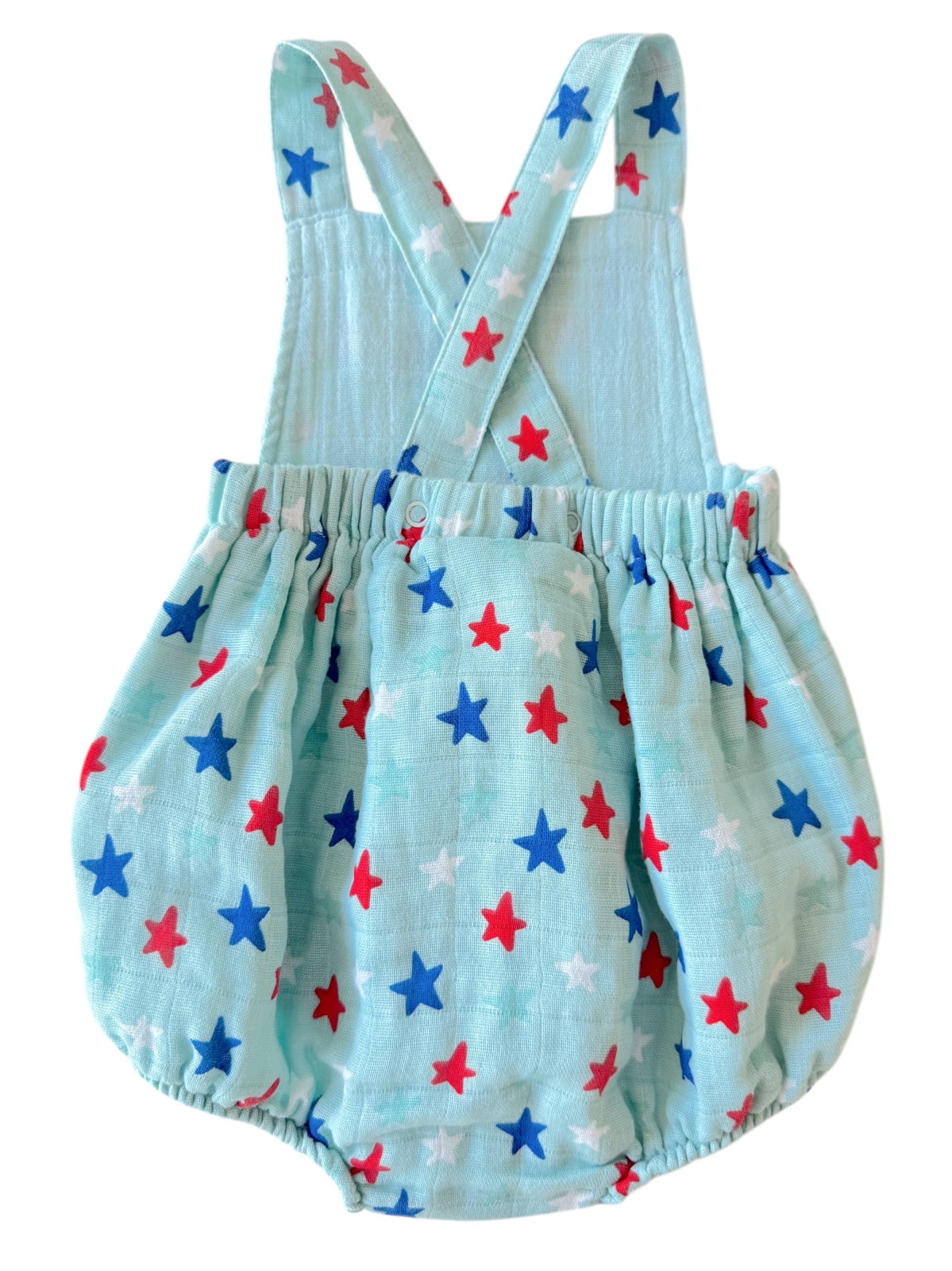 A light blue baby romper with red, white, and blue star patterns and crisscross straps in the back.