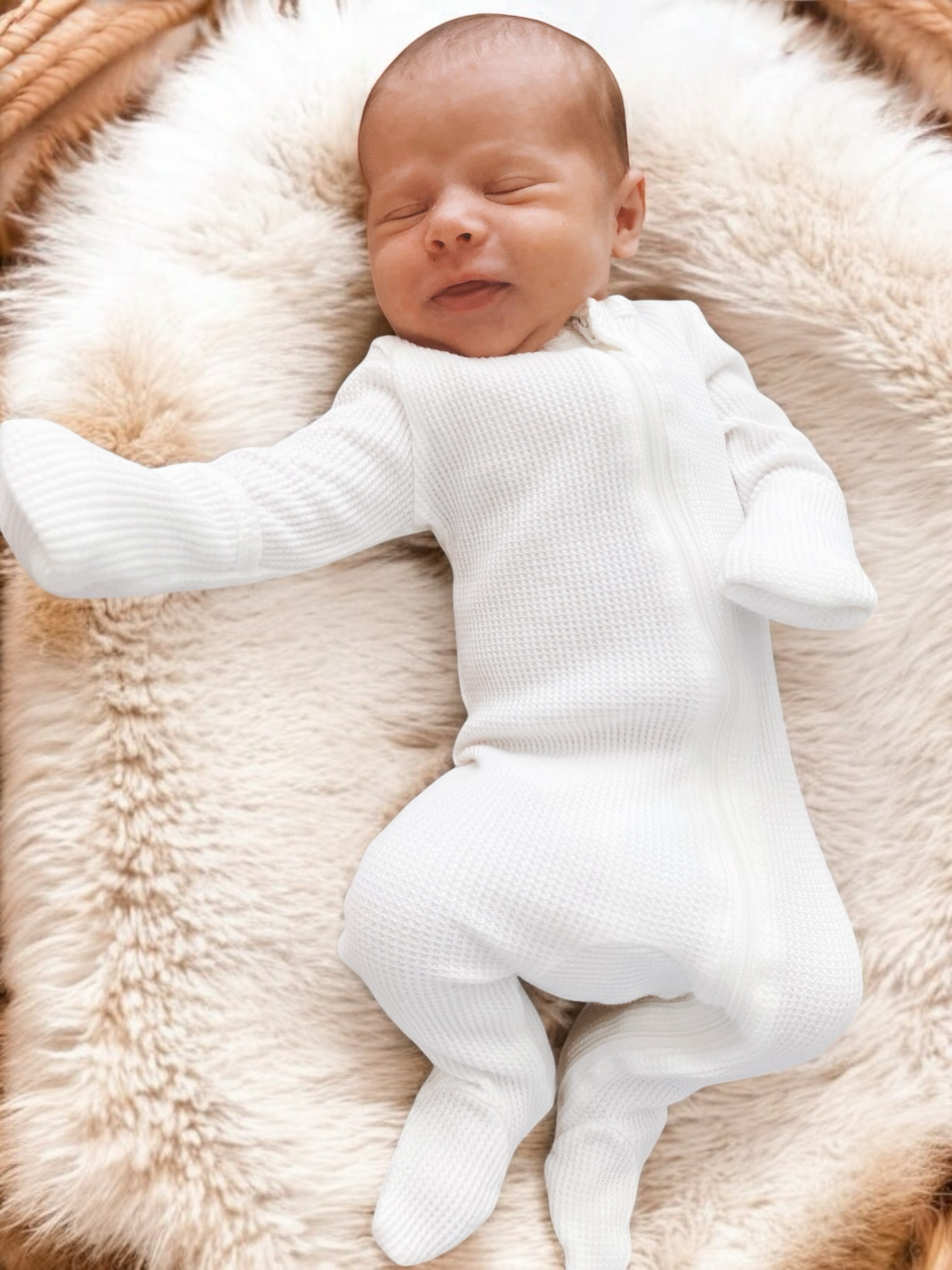 Smiling baby in a white onesie on a fluffy blanket, enjoying a cozy moment.