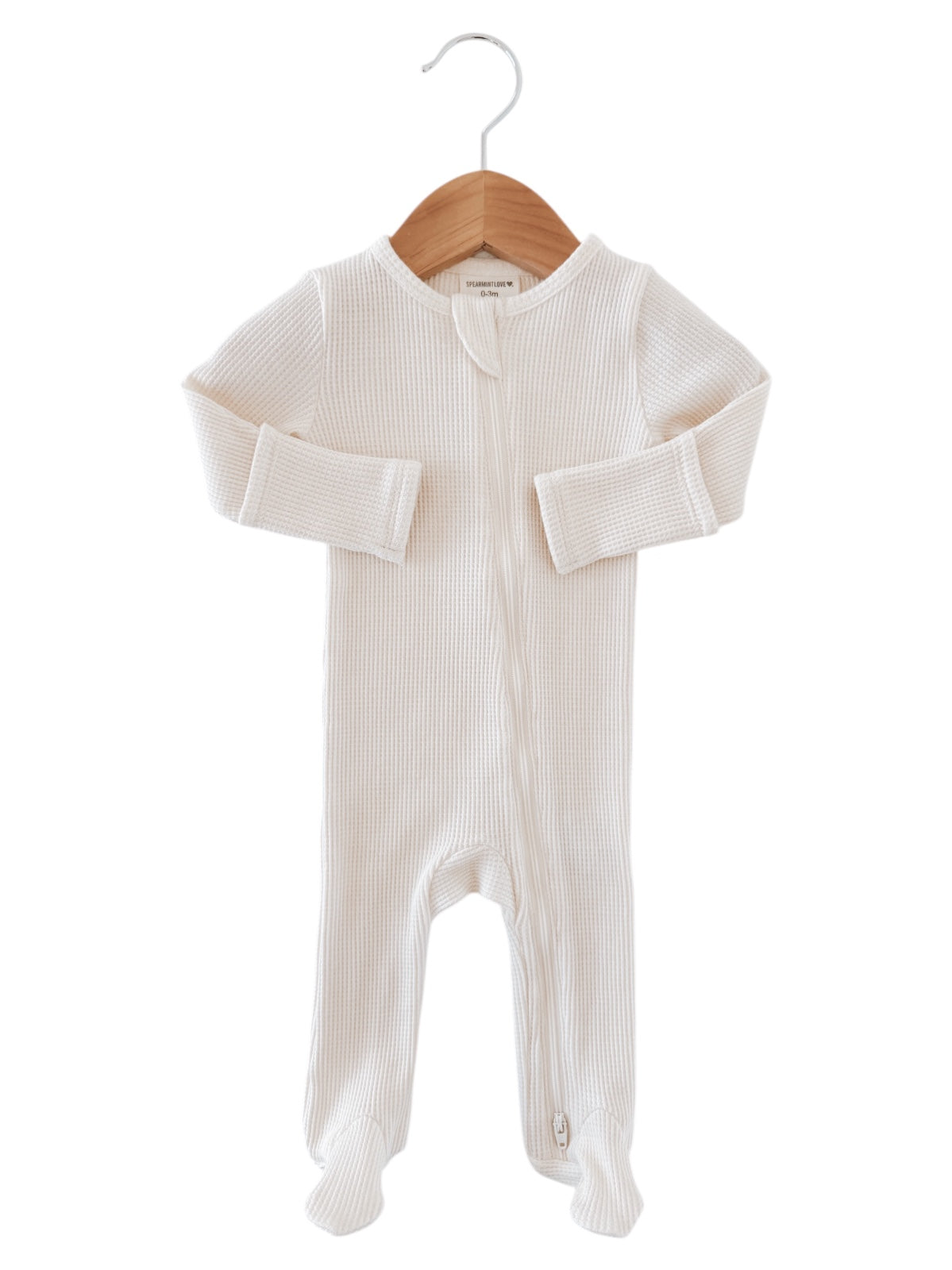 White infant onesie hanging on a wooden hanger, featuring a zipper and textured fabric.