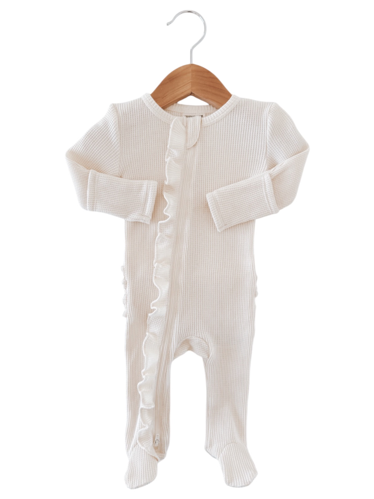 Cream-colored baby onesie with ruffled detailing and front zipper, hanging on a wooden hanger.