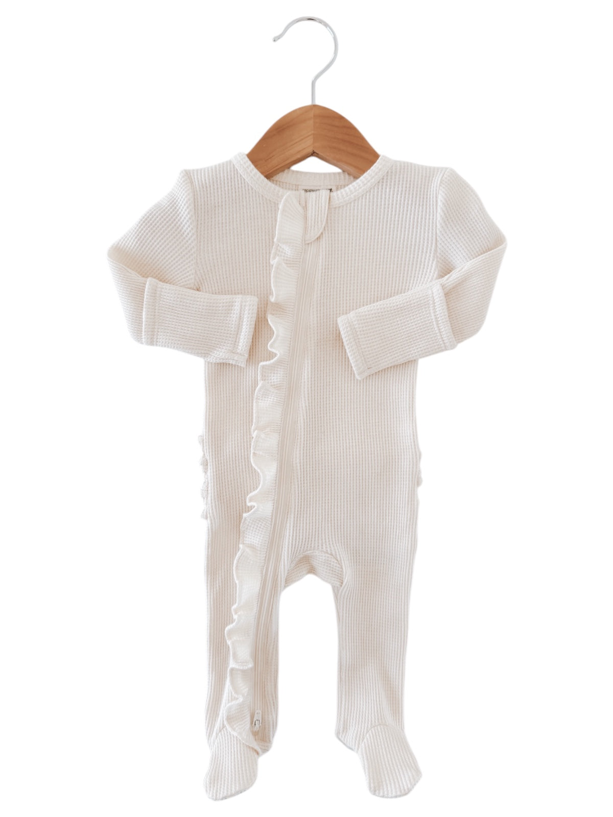 Cream-colored baby onesie with ruffled detailing and front zipper, hanging on a wooden hanger.