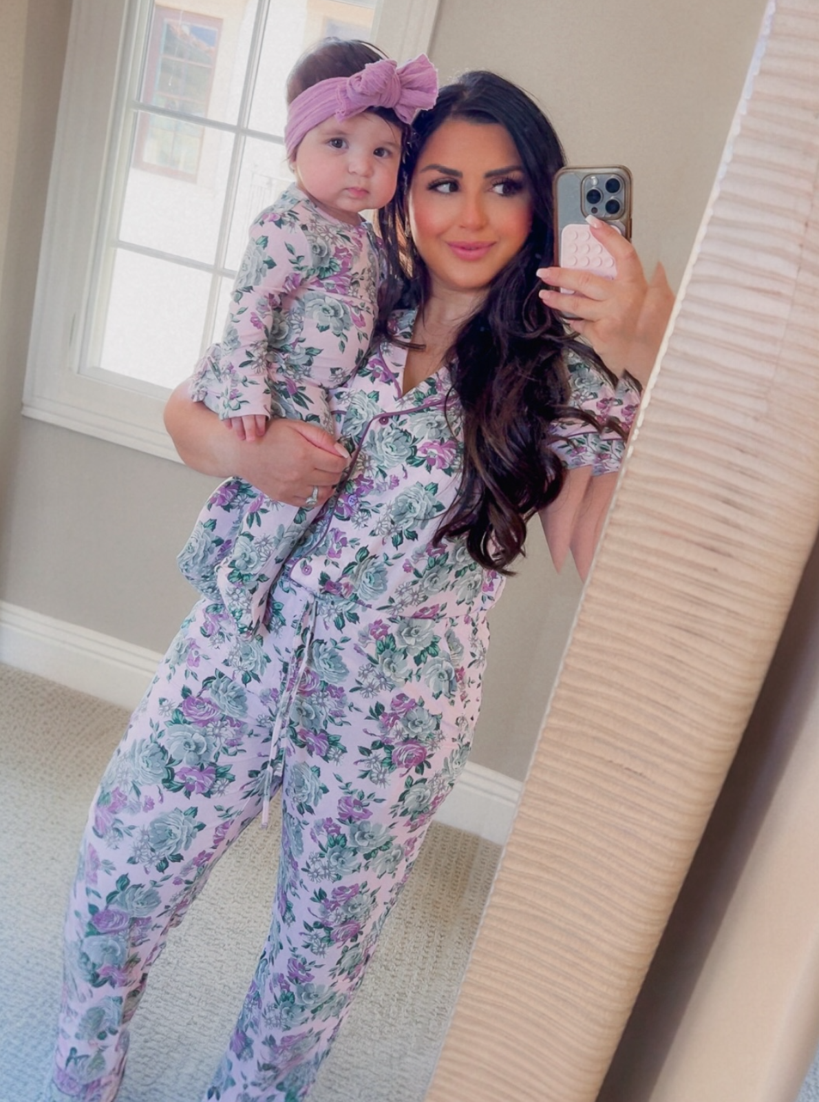 Mother and child in matching floral pajamas, smiling in a mirror selfie at home.