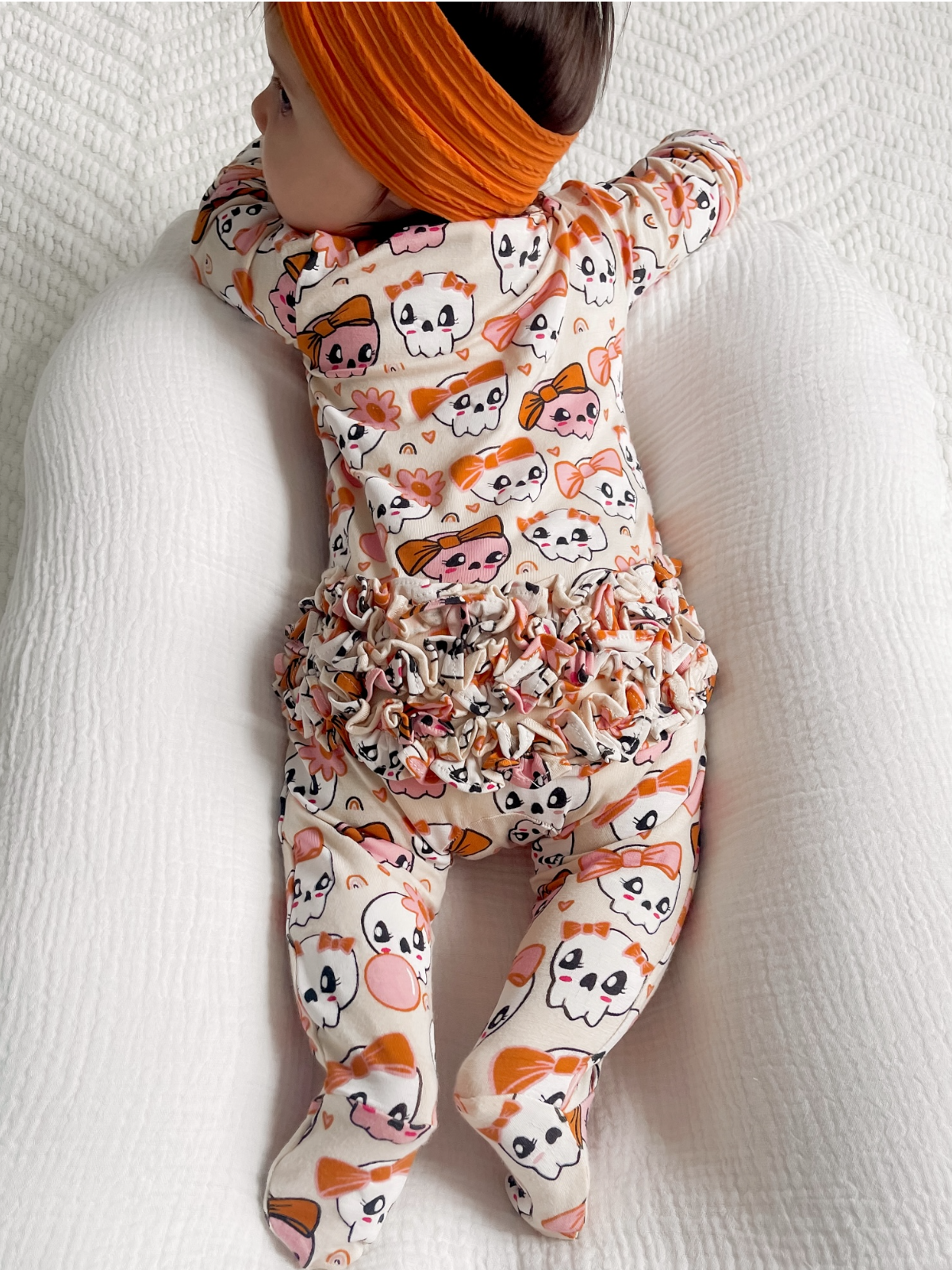Baby in colorful patterned outfit with a matching headband, lying on a soft surface.
