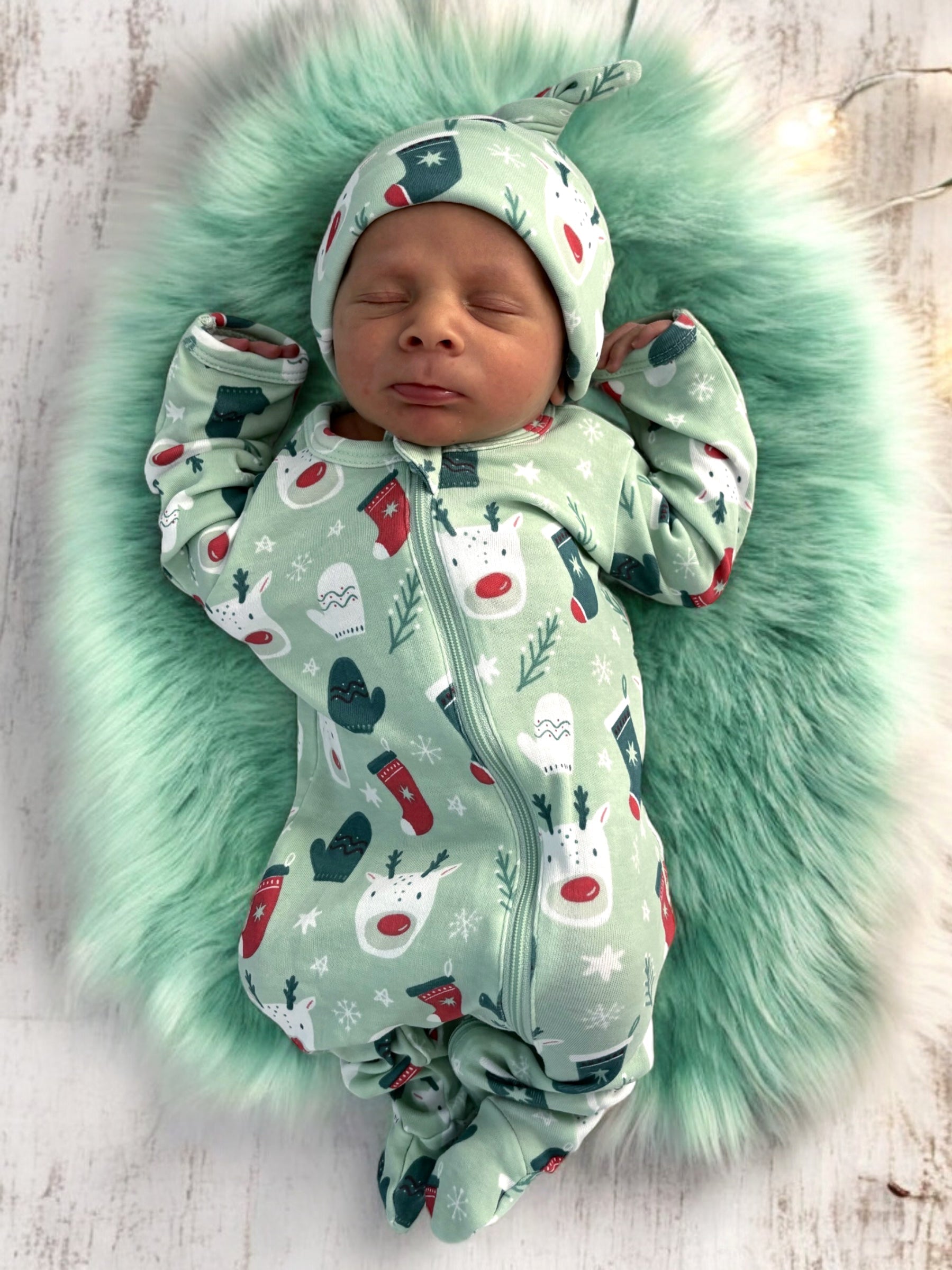 Newborn baby in festive pajamas resting on a soft green blanket with holiday patterns.