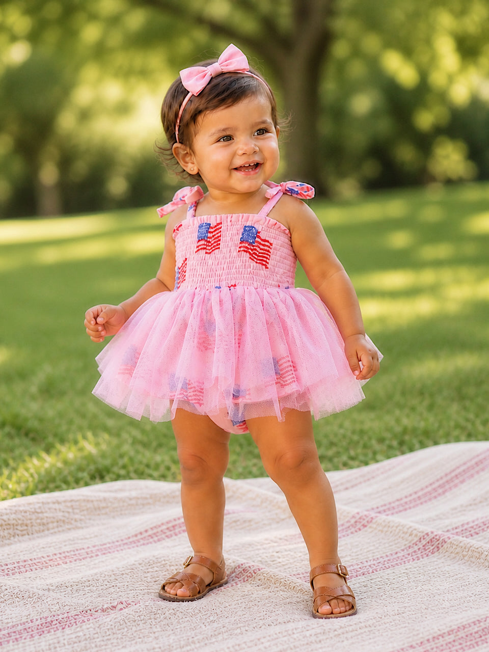 Smiling toddler in a pink dress with bows, standing on grass. Joyful summer atmosphere.