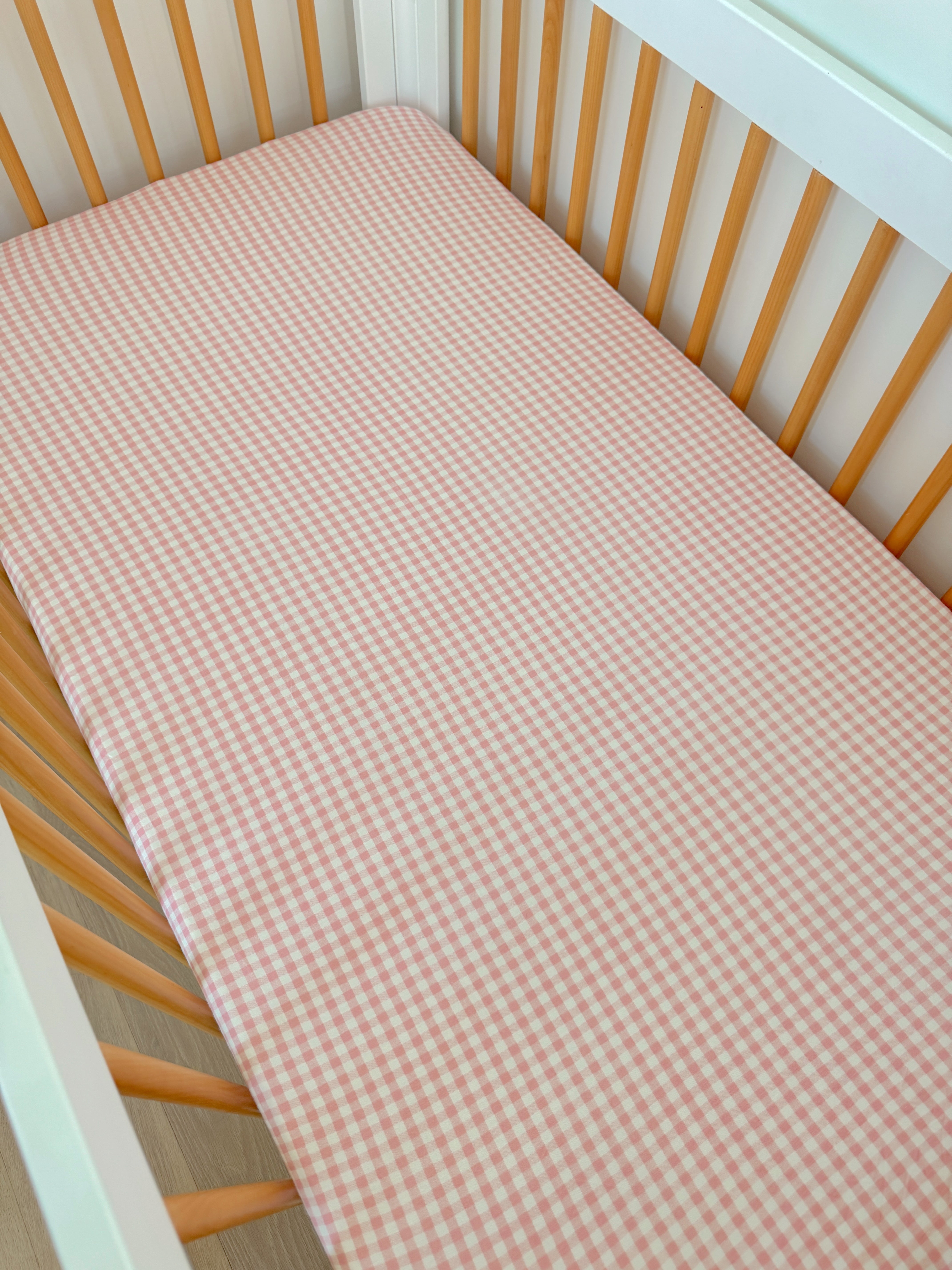 Pink gingham crib sheet on a wooden crib mattress with light wood slats.
