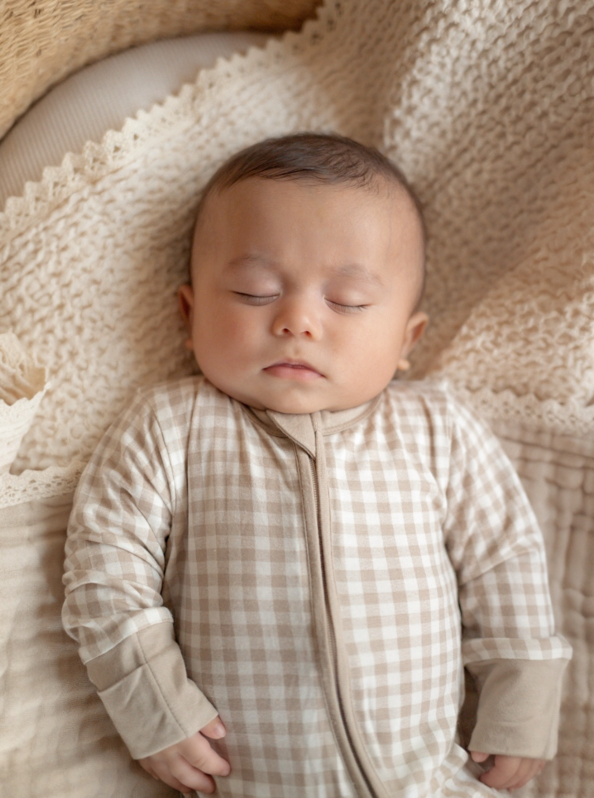 Sleeping baby in a checkered outfit resting on a cozy blanket. Soft, warm colors create a peaceful atmosphere.