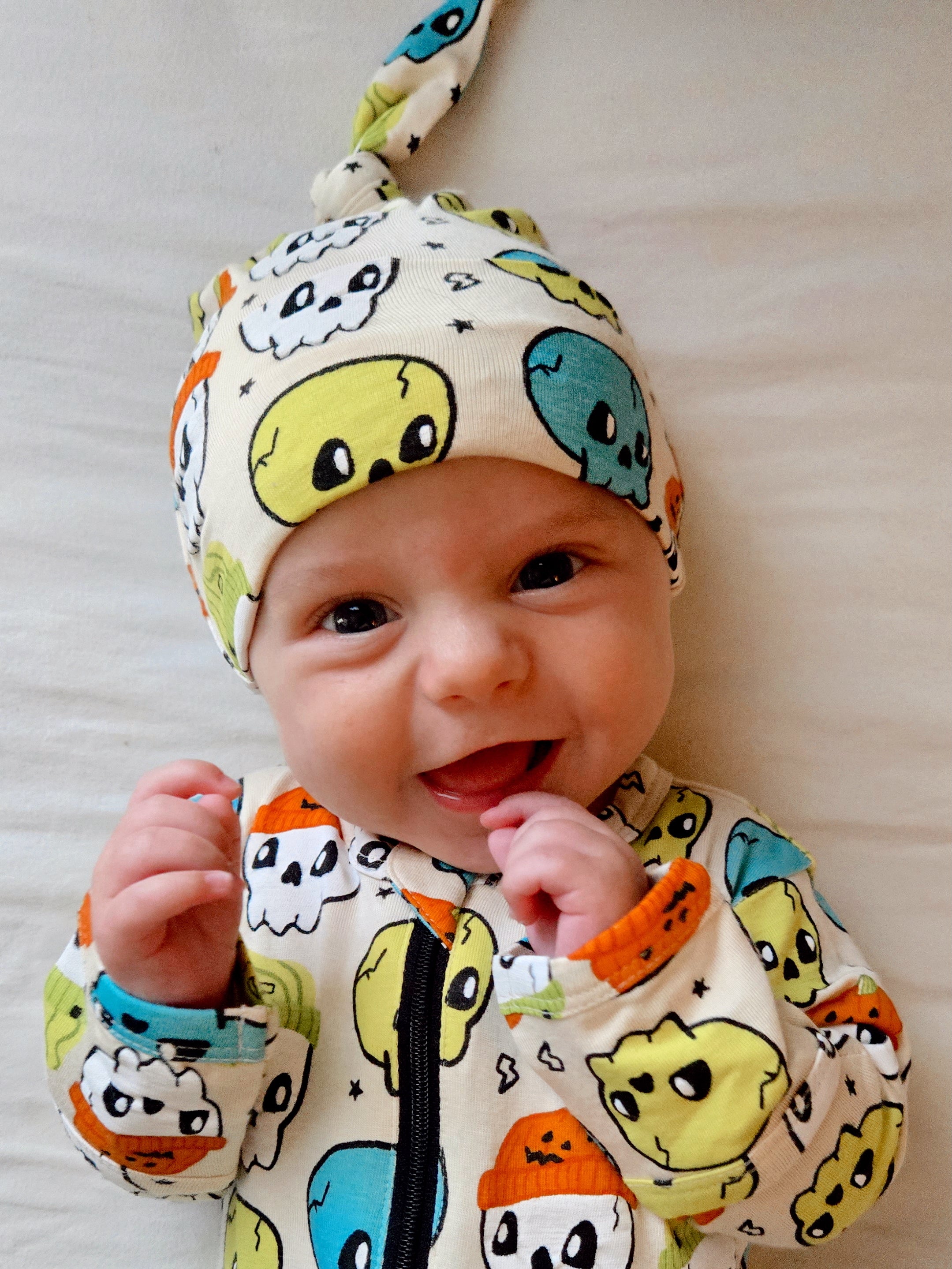 Smiling baby in a colorful ghost-patterned outfit and hat, showcasing a joyful expression.