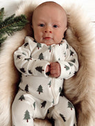 Baby in a tree-patterned onesie, resting on a soft fur blanket with greenery nearby.